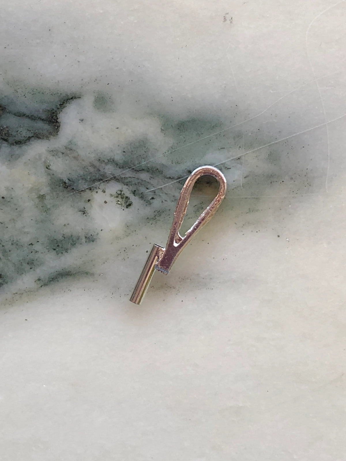 Broochella vertical brooch to necklace converter in silver-tone metal with elongated loop design, photographed on white marble with grey-green veining.