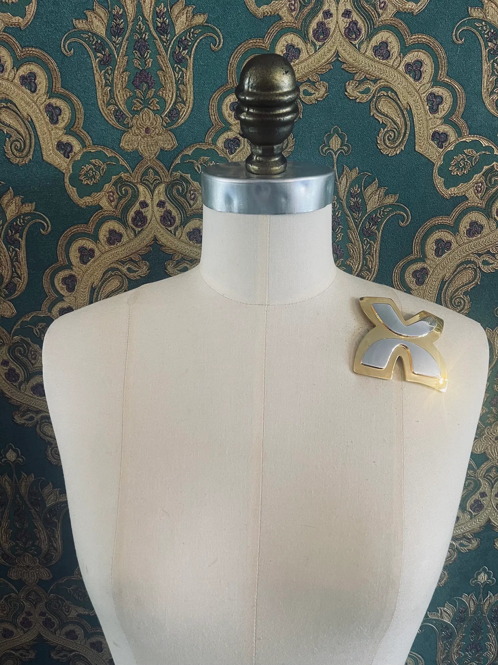 Broochella brooches with meaning freedom brooch in gold and silver metal. Pictured on a mannequin. The background is green and gold damask wallpaper
