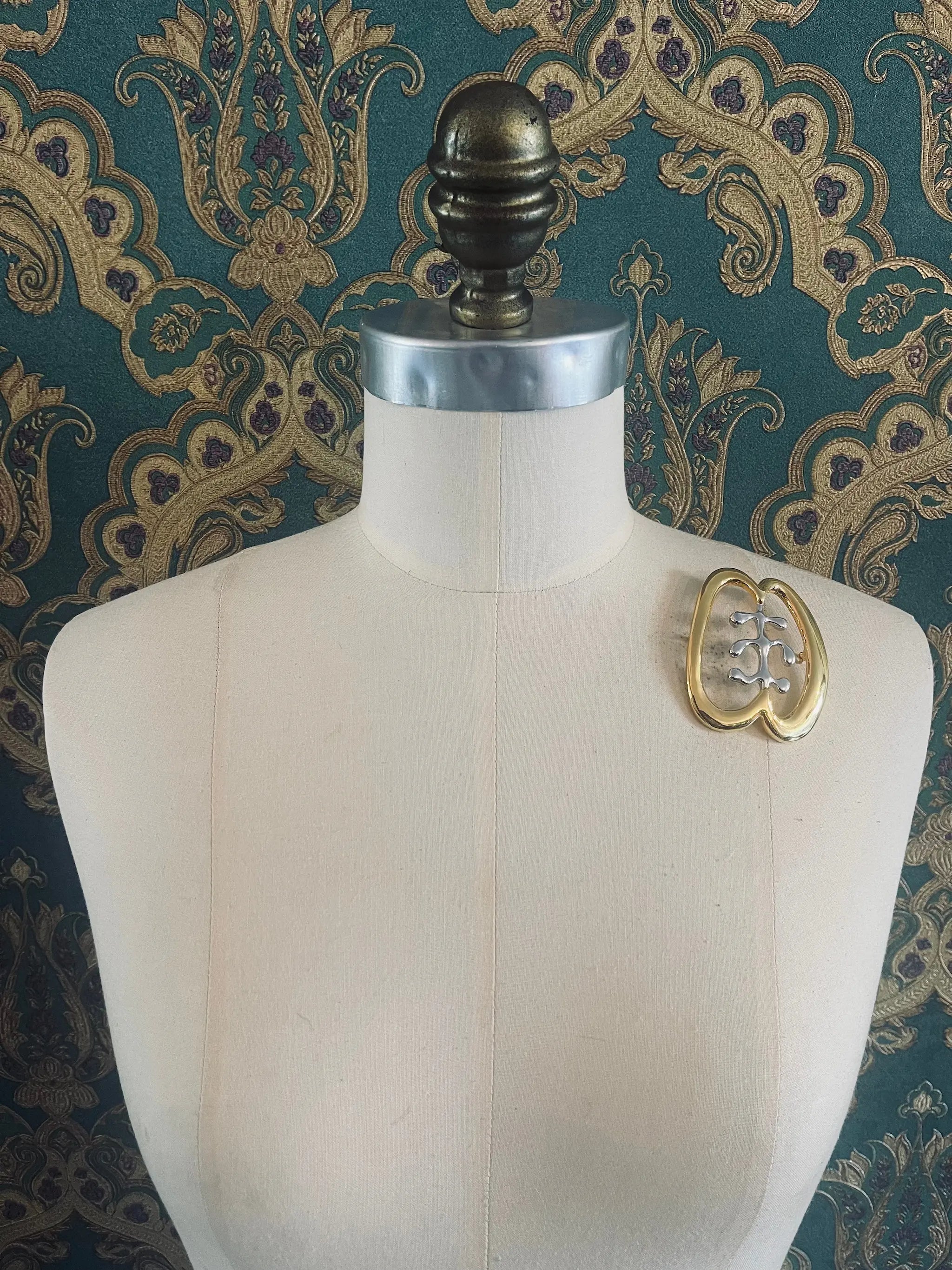 Broochella Brooches with meaning gold and silver metal designer friendship brooch. Pictured on a mannequin. The background is green and gold damask wallpaper