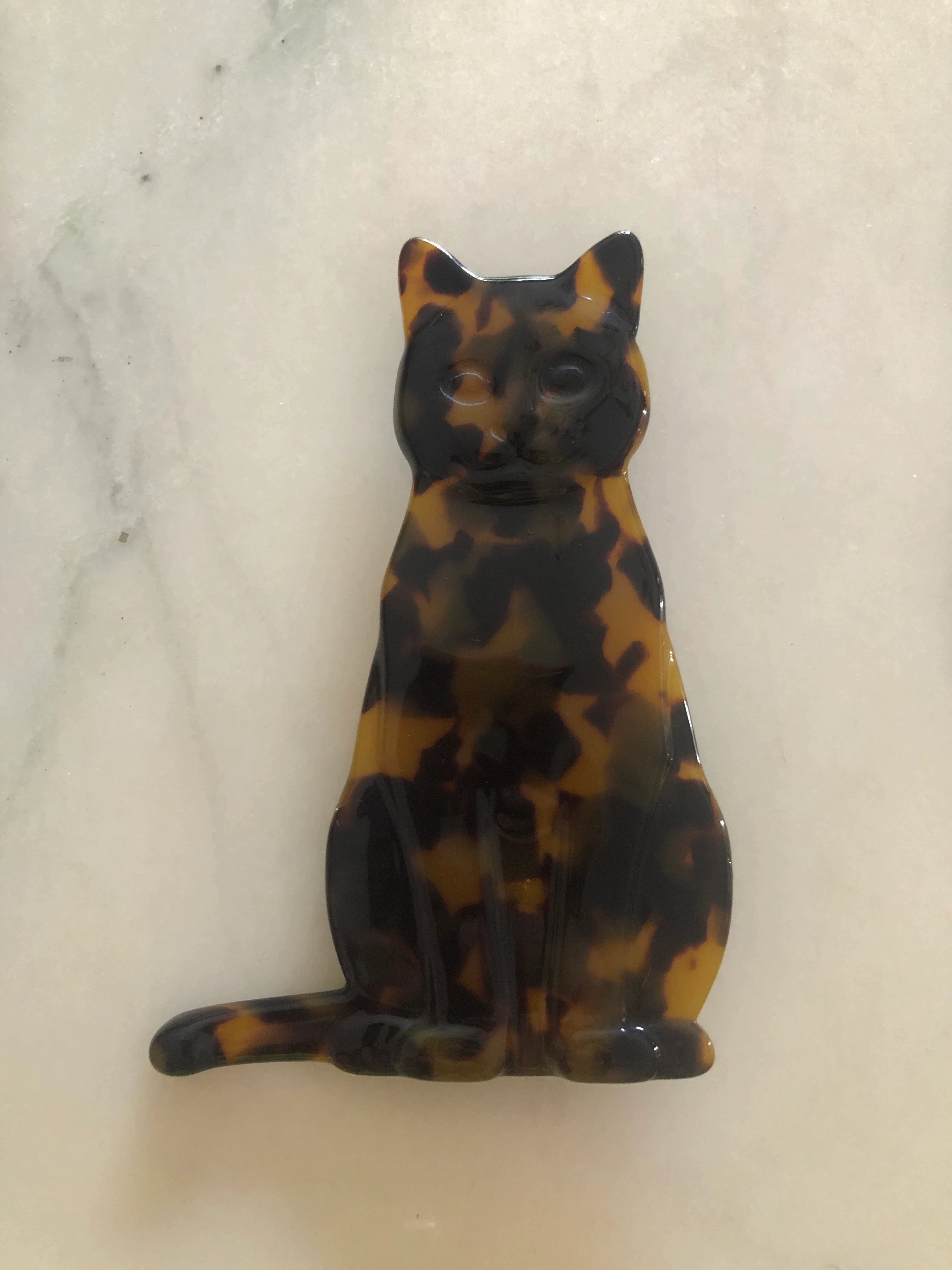 Broochella Men's brown Animalia tortoiseshell giraffe shaped brooch. It is made from Premium Italian cellulose tortoiseshell acetate. It is presented on a beige marble surface.