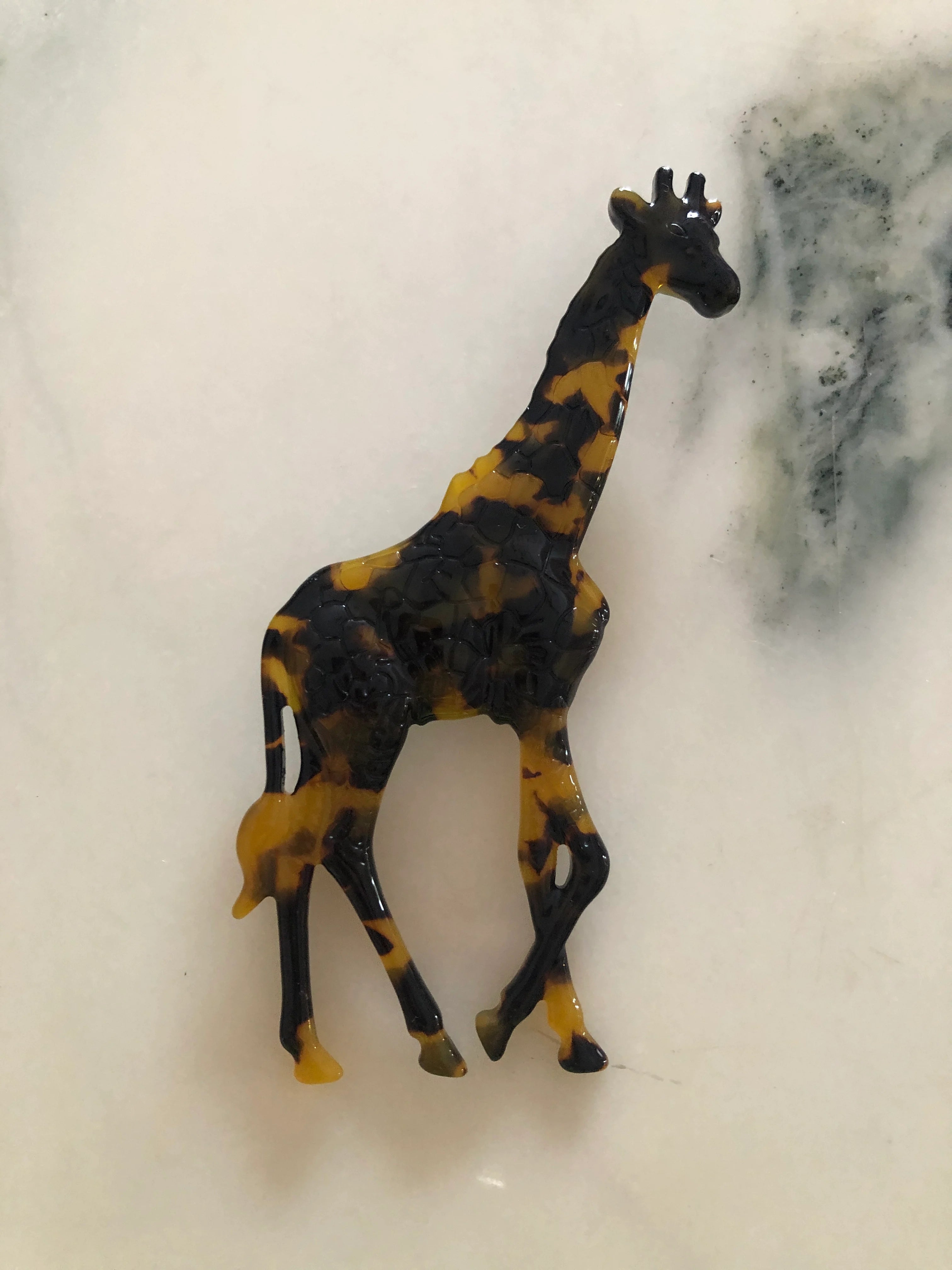 Broochella beige Animalia tortoiseshell giraffe shaped brooch. It is made from Premium Italian cellulose tortoiseshell acetate. It is presented on a white marble surface. 