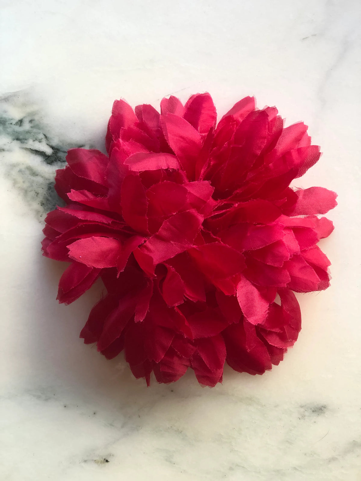 Broochella Calendula Handmade Flower Brooch featuring layered rich red fabric petals in a full sculptural floral design, photographed on a cream marble background.