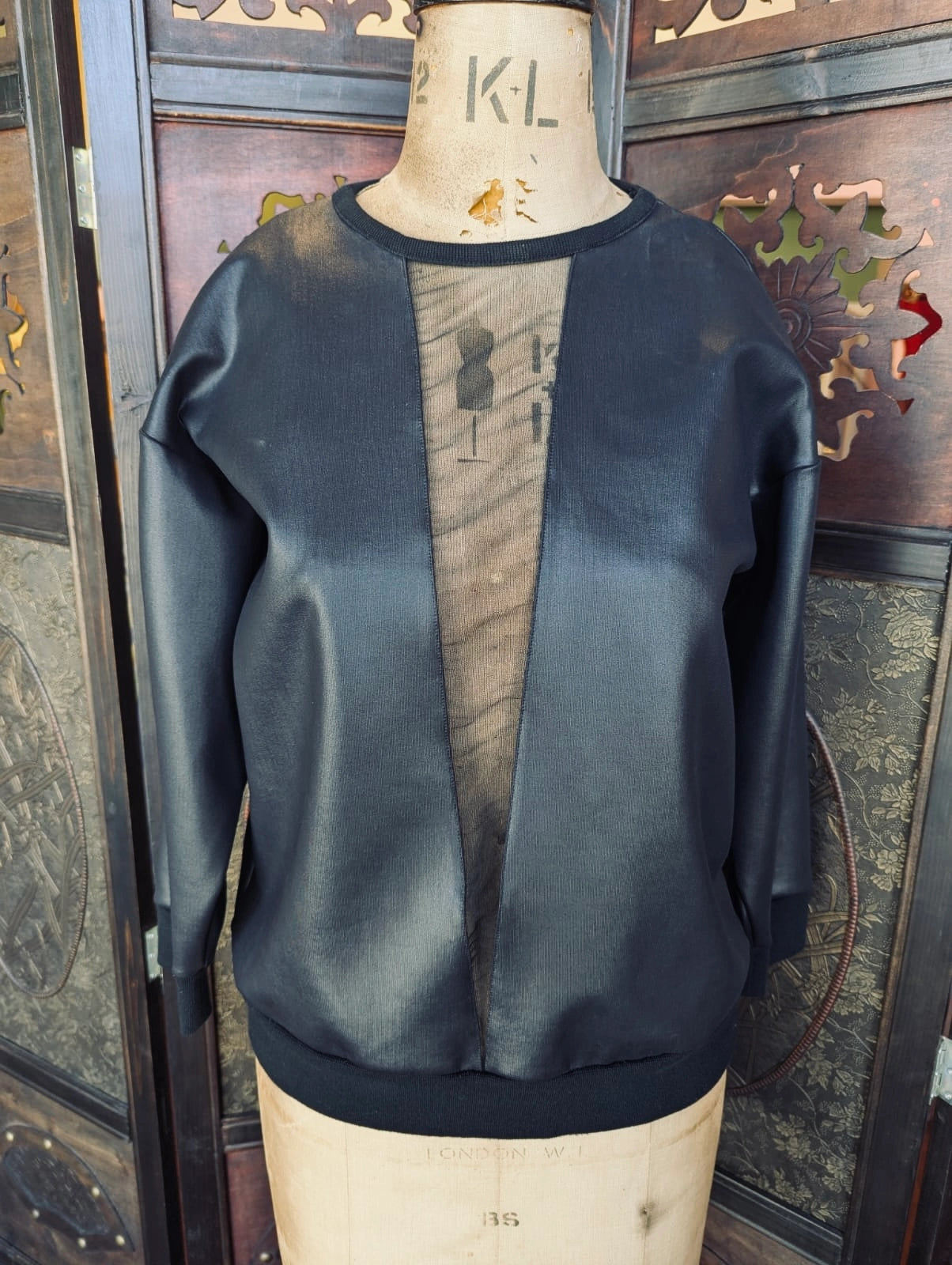 Broochella Christopher Kane  black crewneck sweatshirt with a central mesh panel, displayed on a wooden dress form mannequin in front of a dark wooden screen.