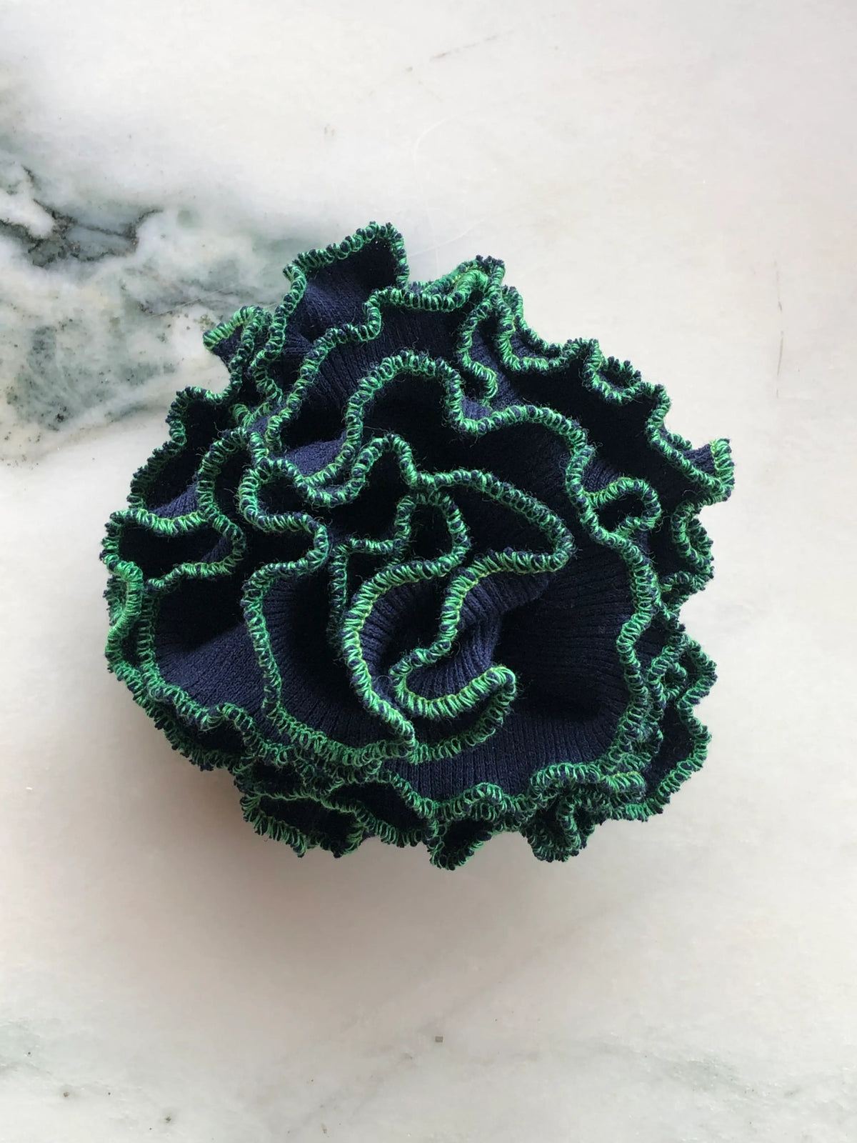 Broochella Corallo Brooch in deep navy with contrasting green ruffled edging, photographed on a white marble background.