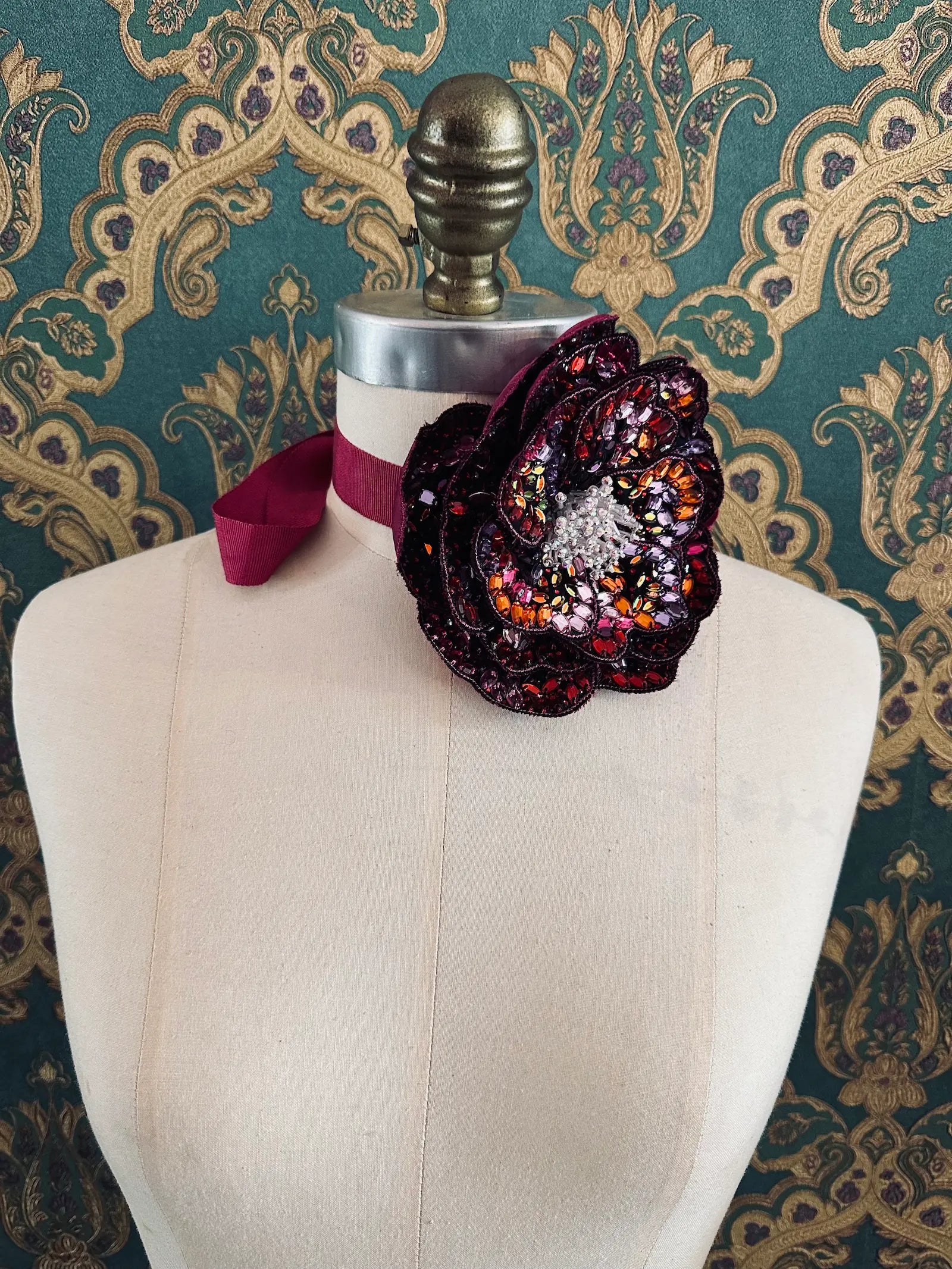 Broochella cristallino hand beaded sequin choker and brooch in pink and burgundy. Pictured on a mannequin. The background is green and gold damask wallpaper.