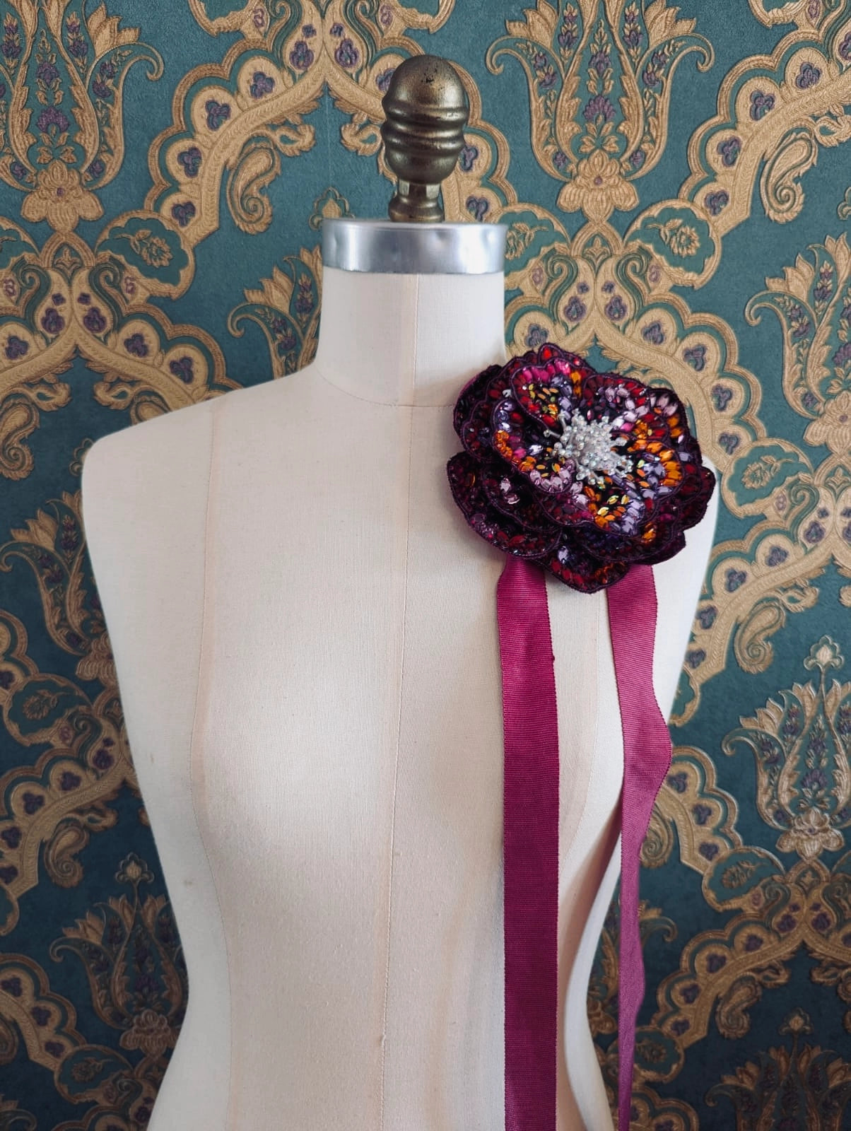 Broochella cristallino hand beaded sequin choker and brooch in pink and burgundy. Pictured on a mannequin. The background is green and gold damask wallpaper.