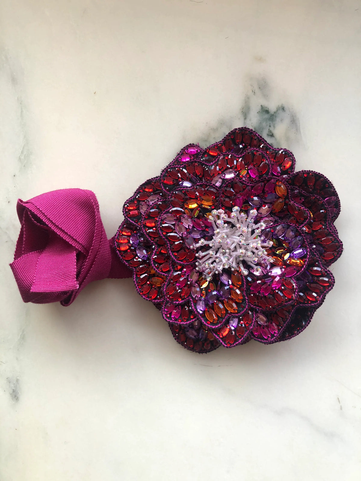 Broochella Cristallino small hand-beaded flower choker and brooch in fuchsia, burgundy, purple and orange crystals with a beaded centre and matching ribbon, photographed on white marble.