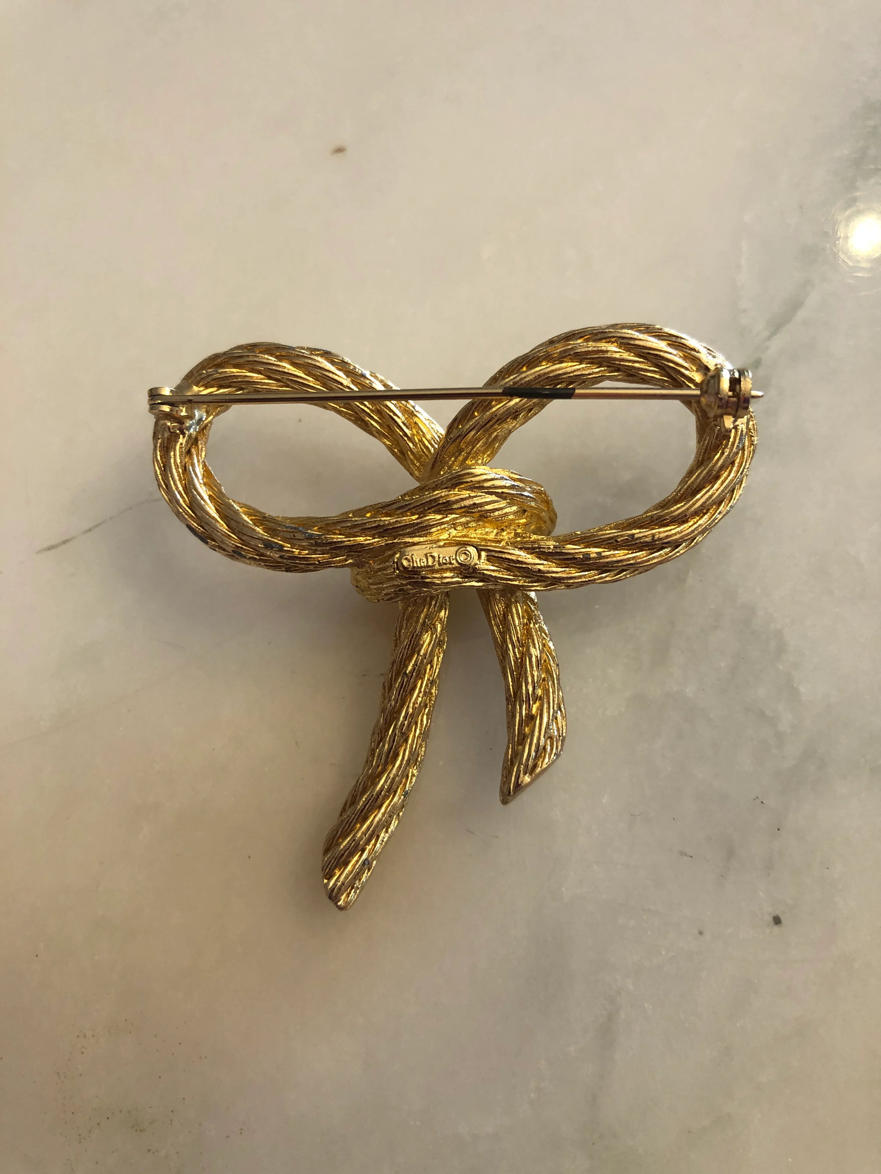 Broochella vintage authentic dior costume bow brooch in gold twisted metal rope. The background is white marble