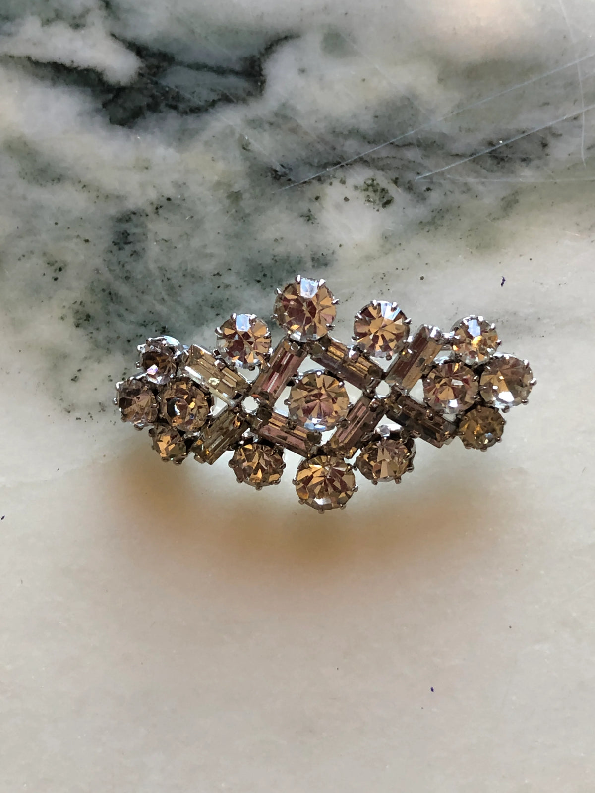 Broochella Donatella Vintage Crystal Lattice Brooch featuring round and baguette-cut clear crystals in an open geometric silver-tone setting on a cream and grey marble background.