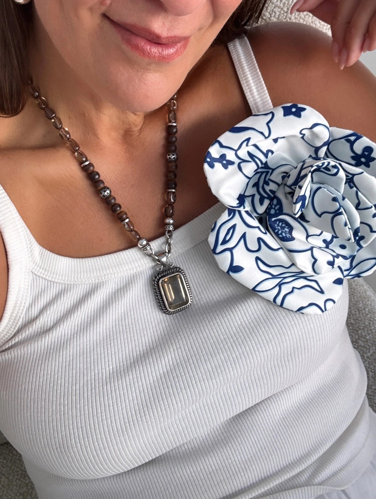 A model with dark hair is wearing a white tank top and a chunky brown and silver necklace. Pinned to her chest is the Broochella Electra flower brooch and choker.