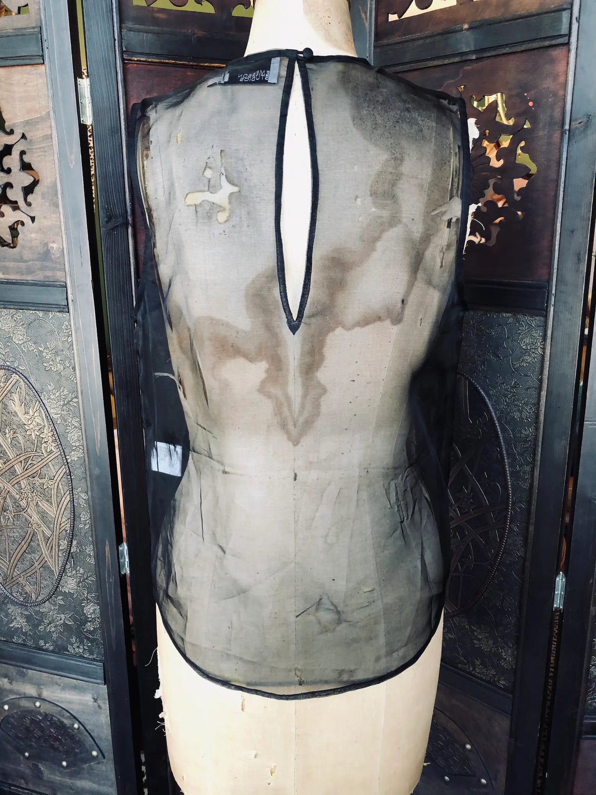 Broochella Emerson studios, Small, 100% Silk, Black, Sleeveless design, Sheer silk finish, Front panel pockets. Keyhole back detail. It is presented on a vintage mannequin. The background is a ornate, vintage, dark wood room divider. 