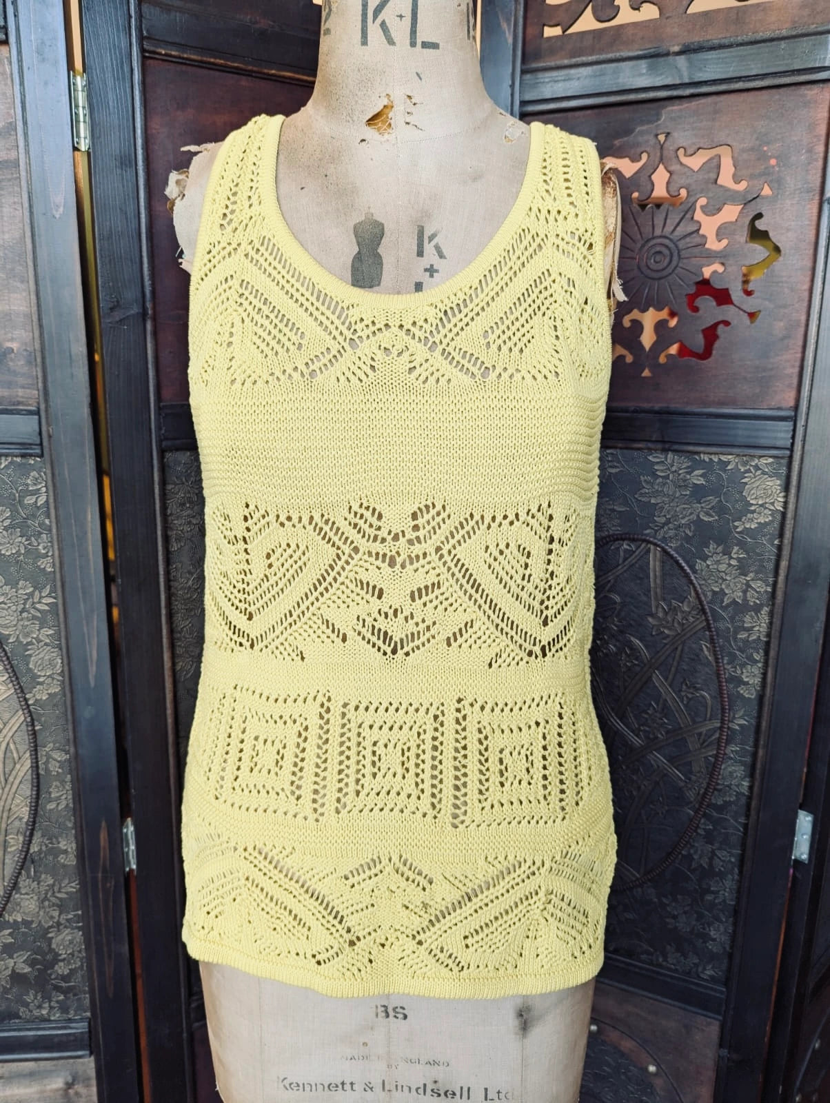 A Broochella authentic designer Emilio Pucci yellow open-knit sleeveless top displayed on a vintage wooden dress form mannequin, set against a dark carved wooden screen.