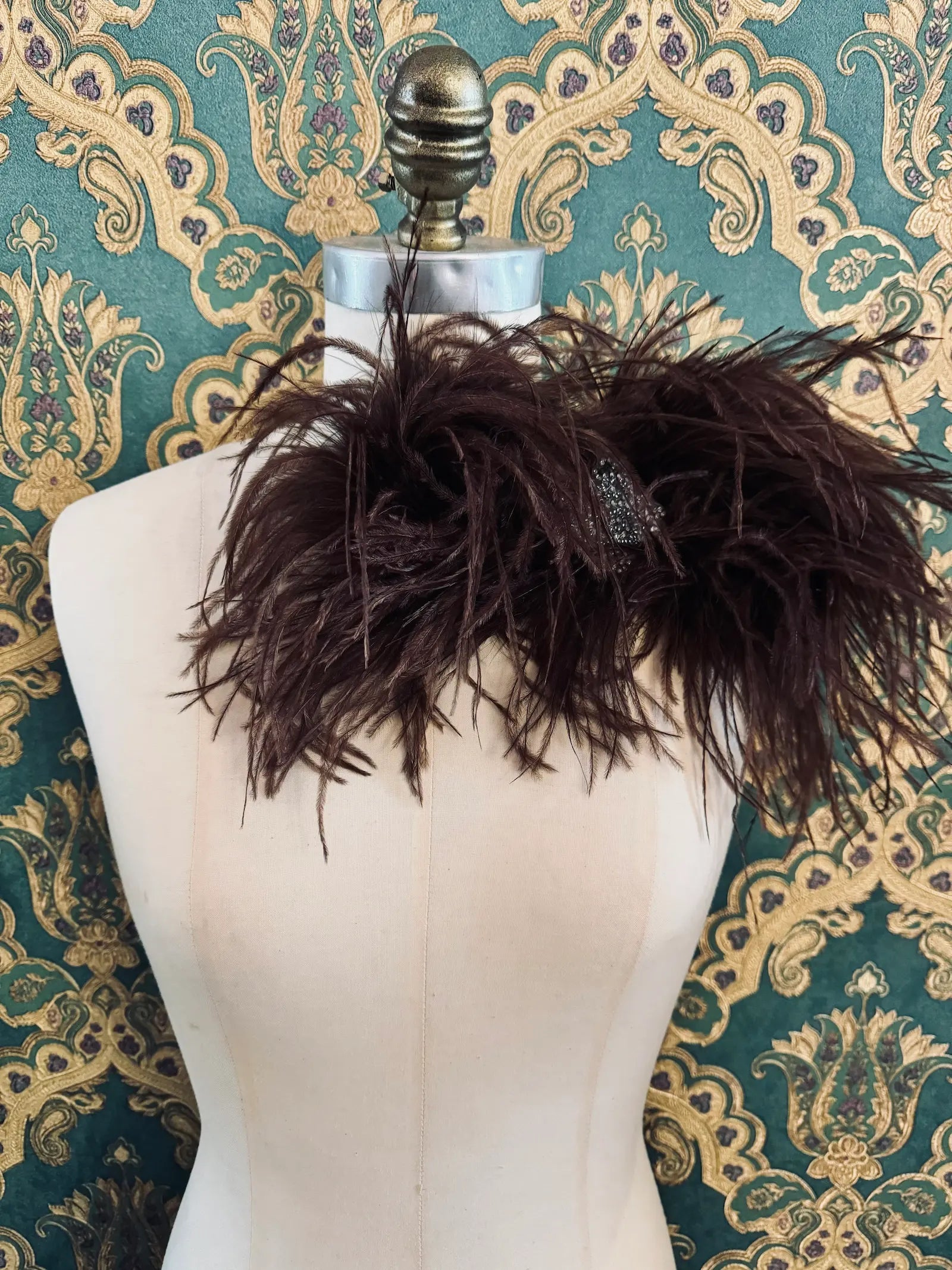 Broochella brown handmade large feather bow brooch with embellished centre.  Pictured on a mannequin.  The background is green and gold damask wallpaper.