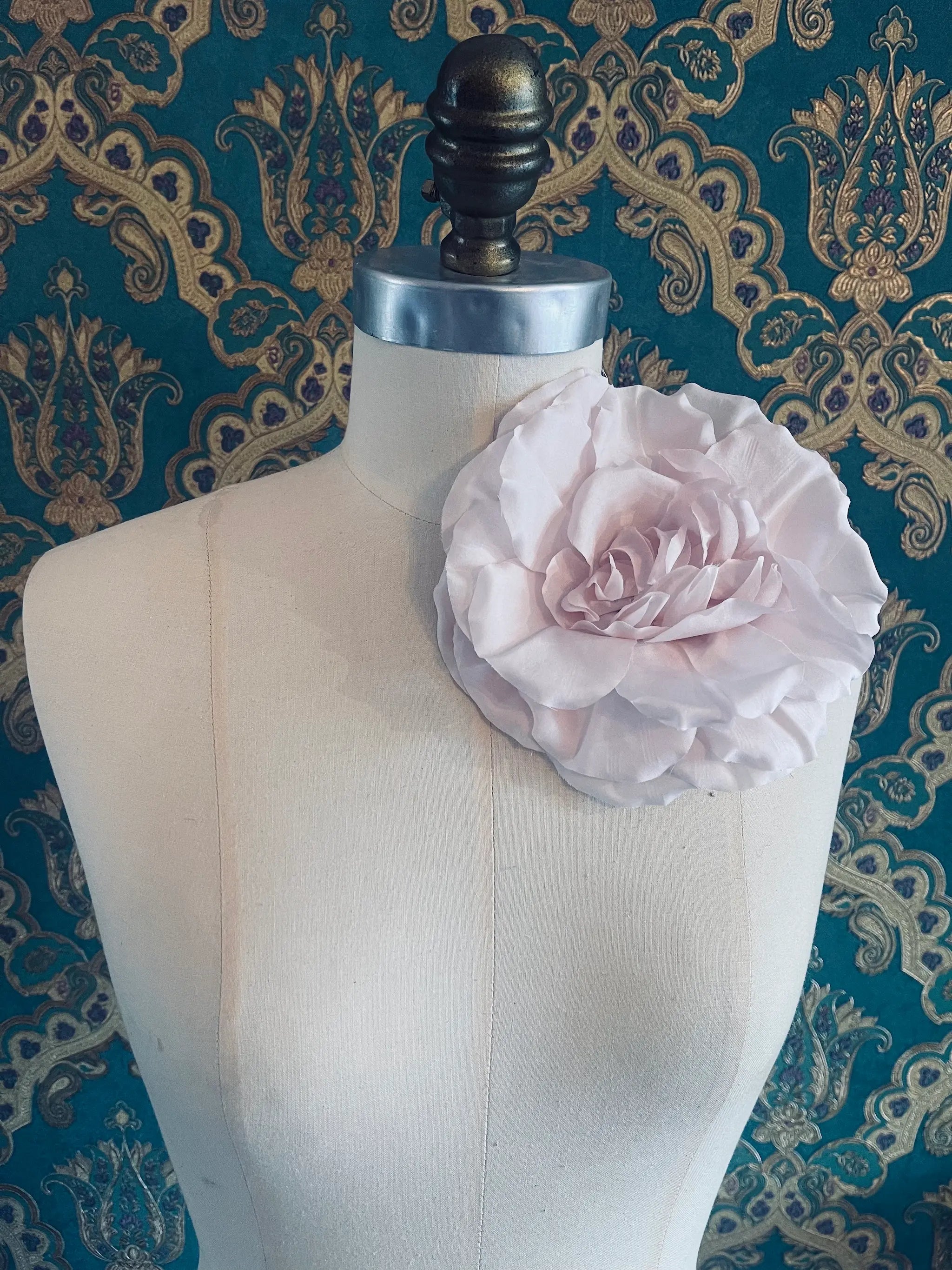 Broochella Femmina handmade designer fabric flower brooch in pink. Pictured on a mannequin. The background is green and gold damask wallpaper