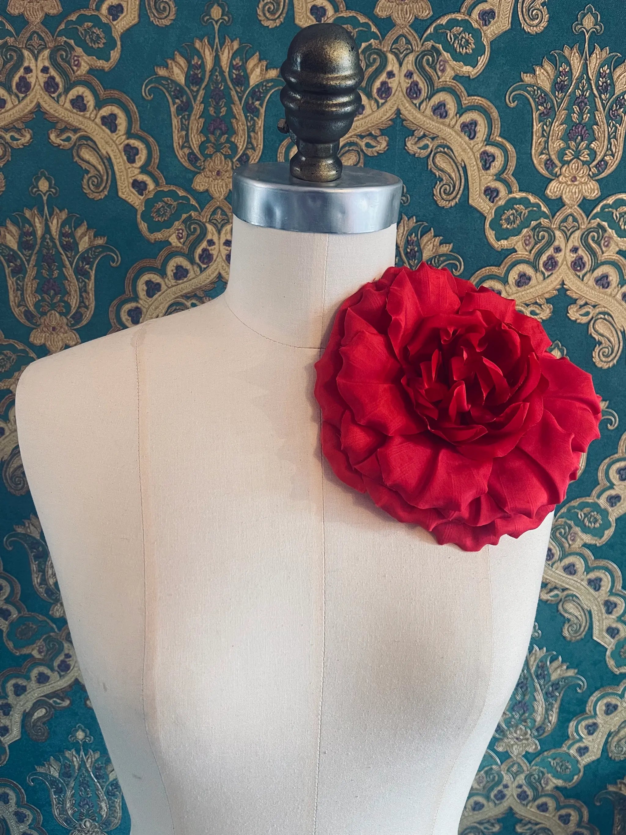 Broochella Femmina handmade designer fabric flower brooch in red. Pictured on a mannequin. The background is green and gold damask wallpaper