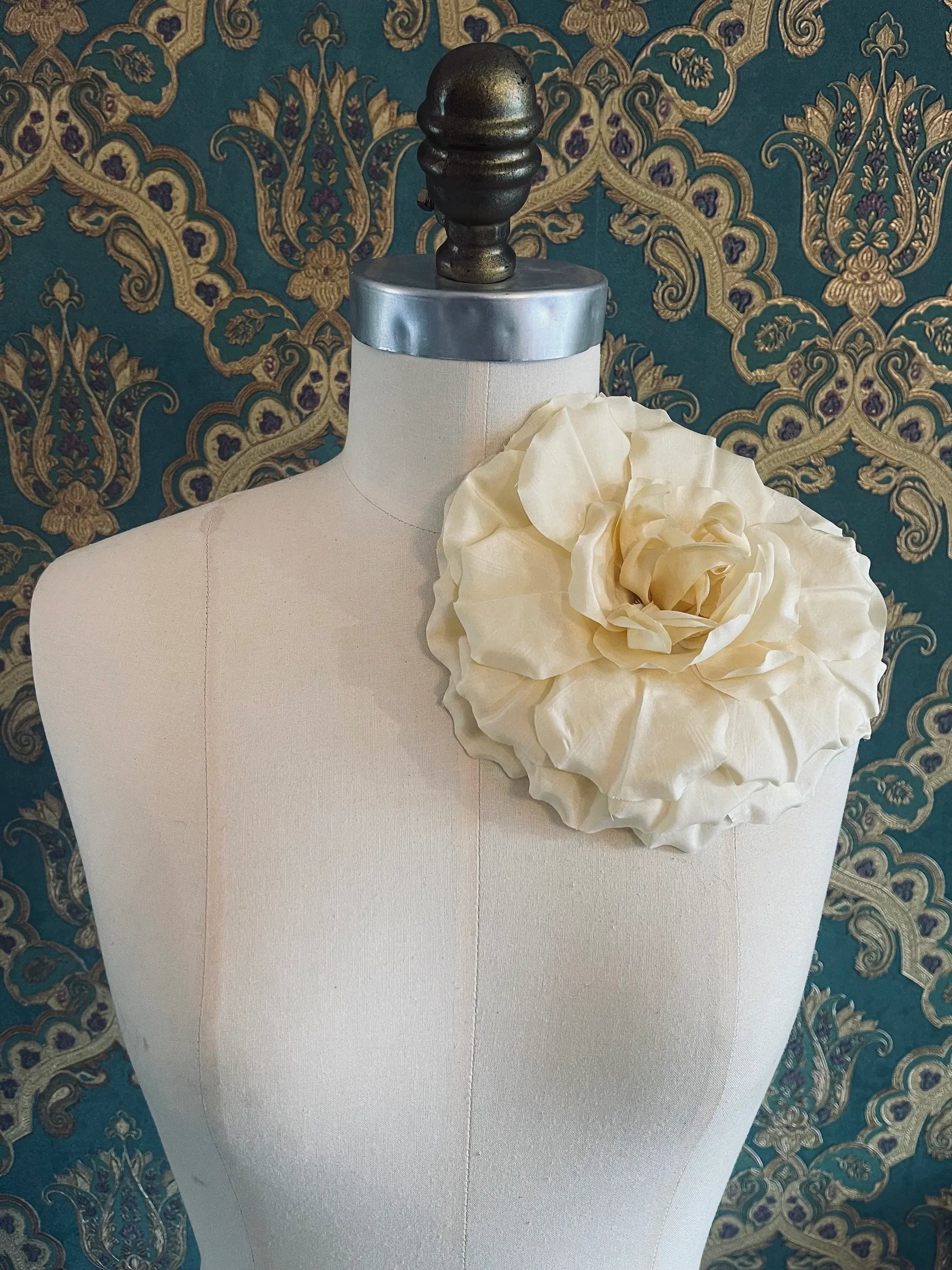 Broochella Femmina handmade designer fabric flower brooch in yellow. Pictured on a mannequin. The background is green and gold damask wallpaper