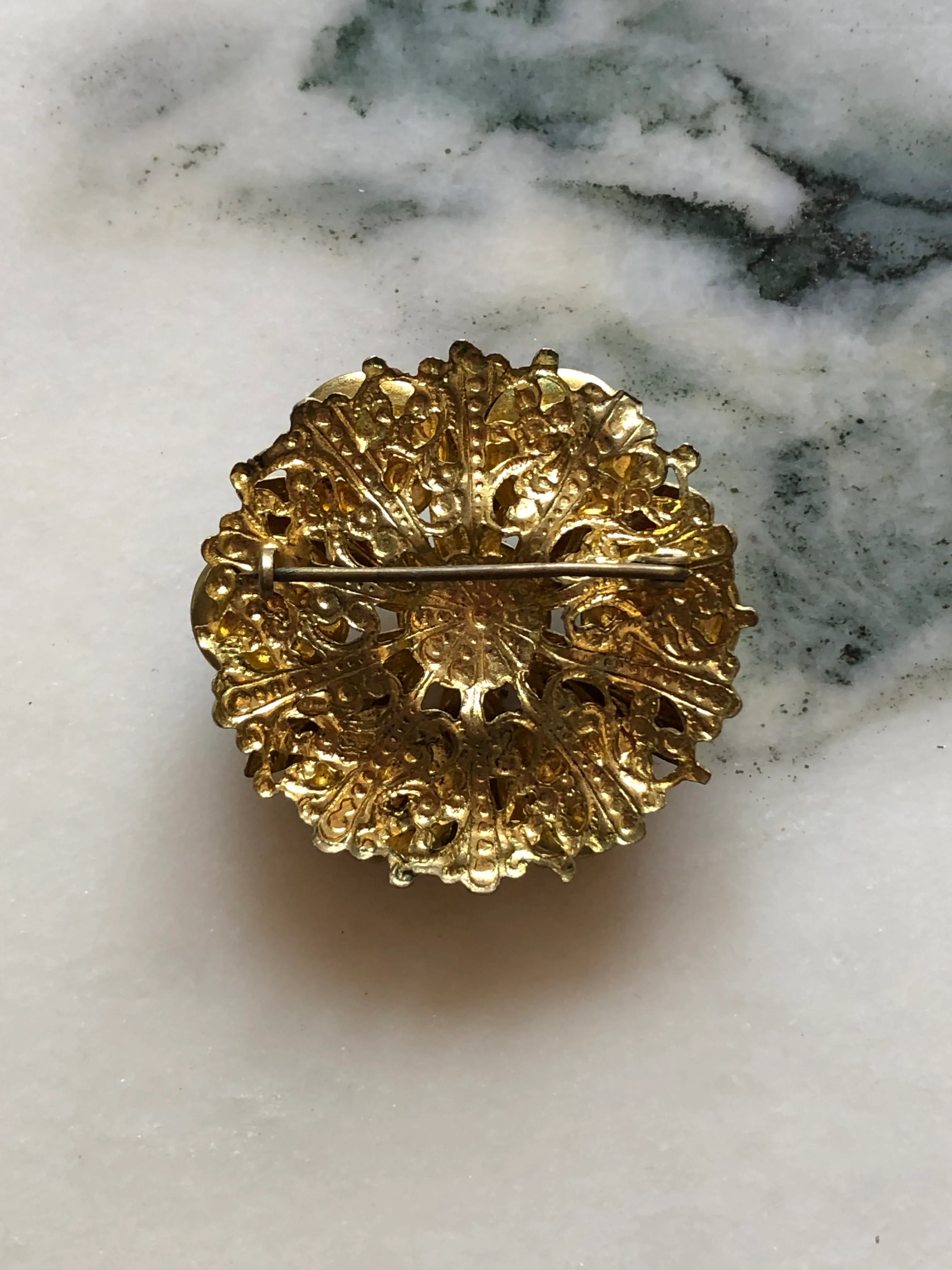 The back view of Broochella Fiamma Boema vintage Broochella Czech brooch with red-orange marbled glass cabochons and sculpted gold-tone leaves. The background is white marble.