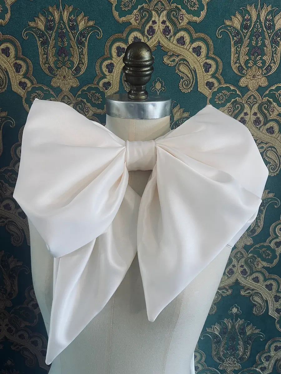 Broochella Fiocco Large ivory handmade designer bow Pictured on a mannequin. The background is green and gold damask wallpaper