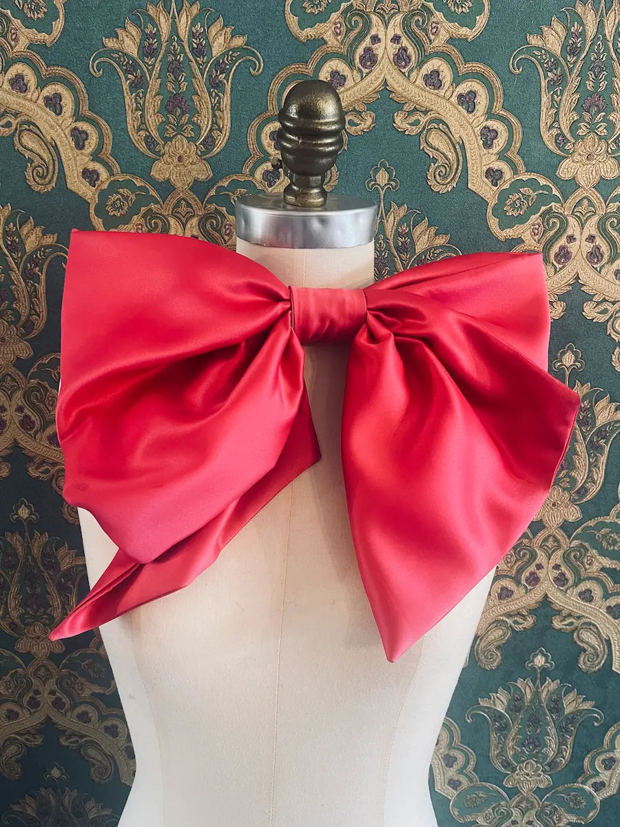 Broochella Fiocco Large pink satin handmade designer bow Pictured on a mannequin. The background is green and gold damask wallpaper