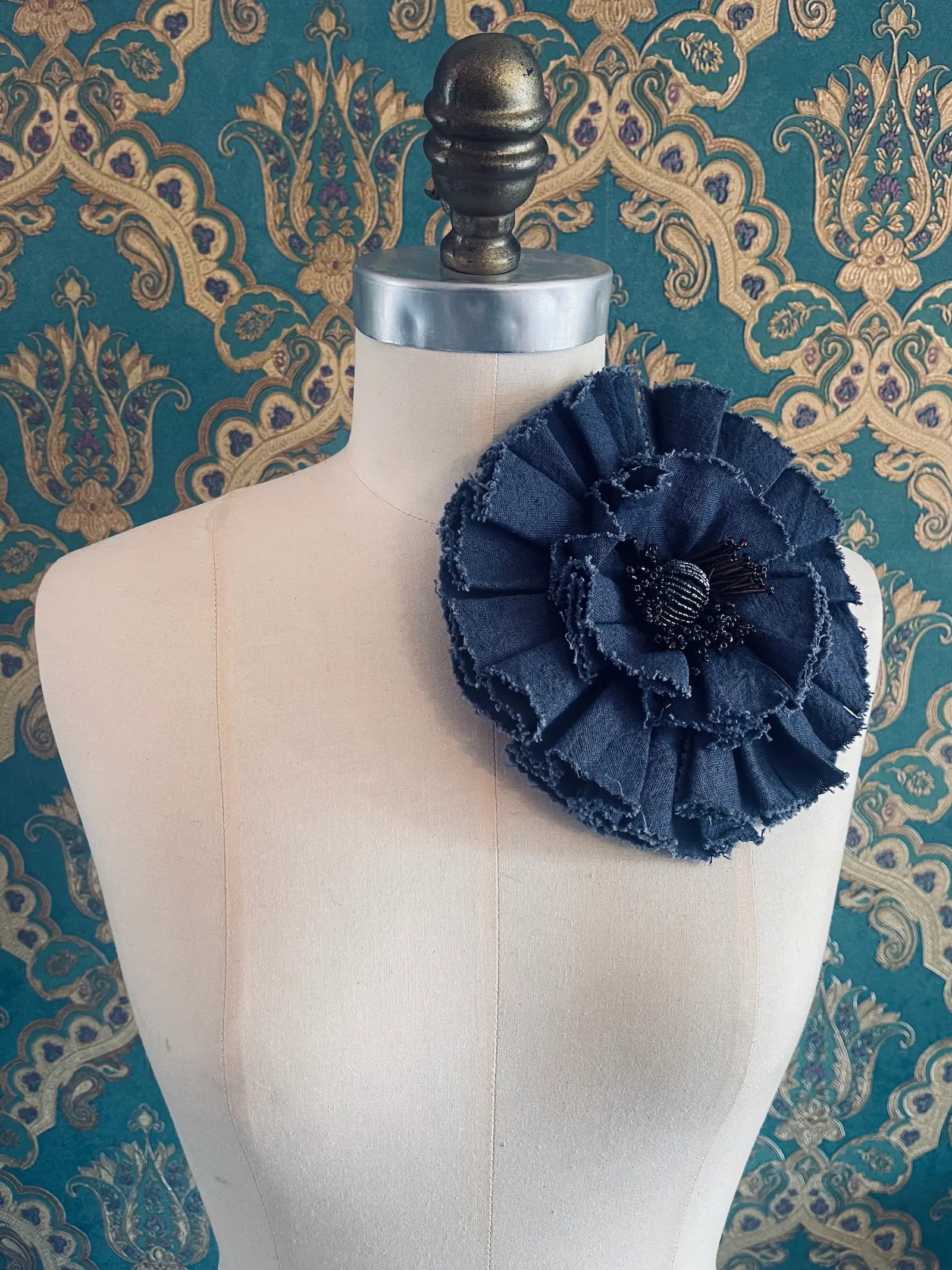Broochella fiordaliso handmade large fabric flower brooch in red. Styled on a mannequin. The background is green and gold damask wallpaper