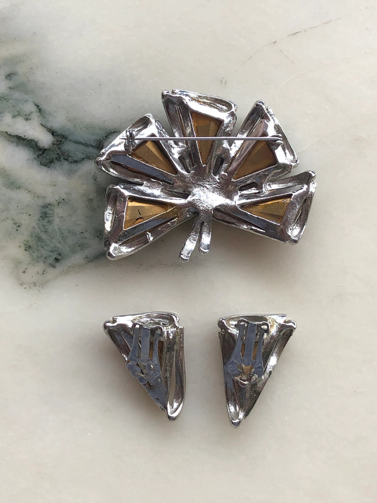 Broochella Sole d’Oro Vintage Brooch back view showing the textured gold-tone leaf construction and traditional pin fastening, photographed on white marble with natural grey-green veining.