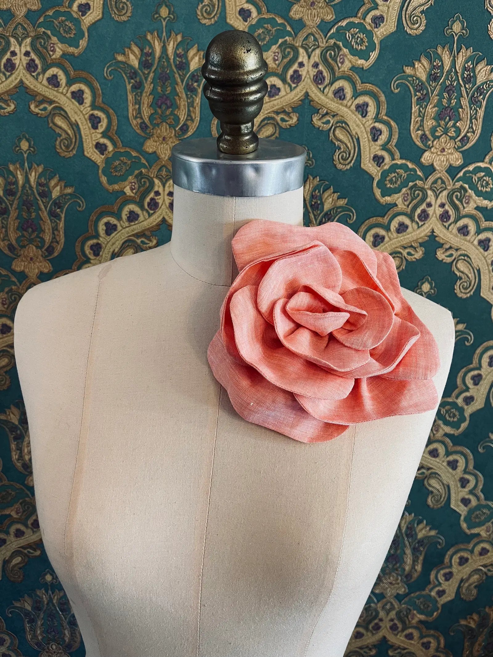 Broochella Florella large handmade linen flower brooch in orange. Pictured on a mannequin. The background is green and gold damask wallpaper.