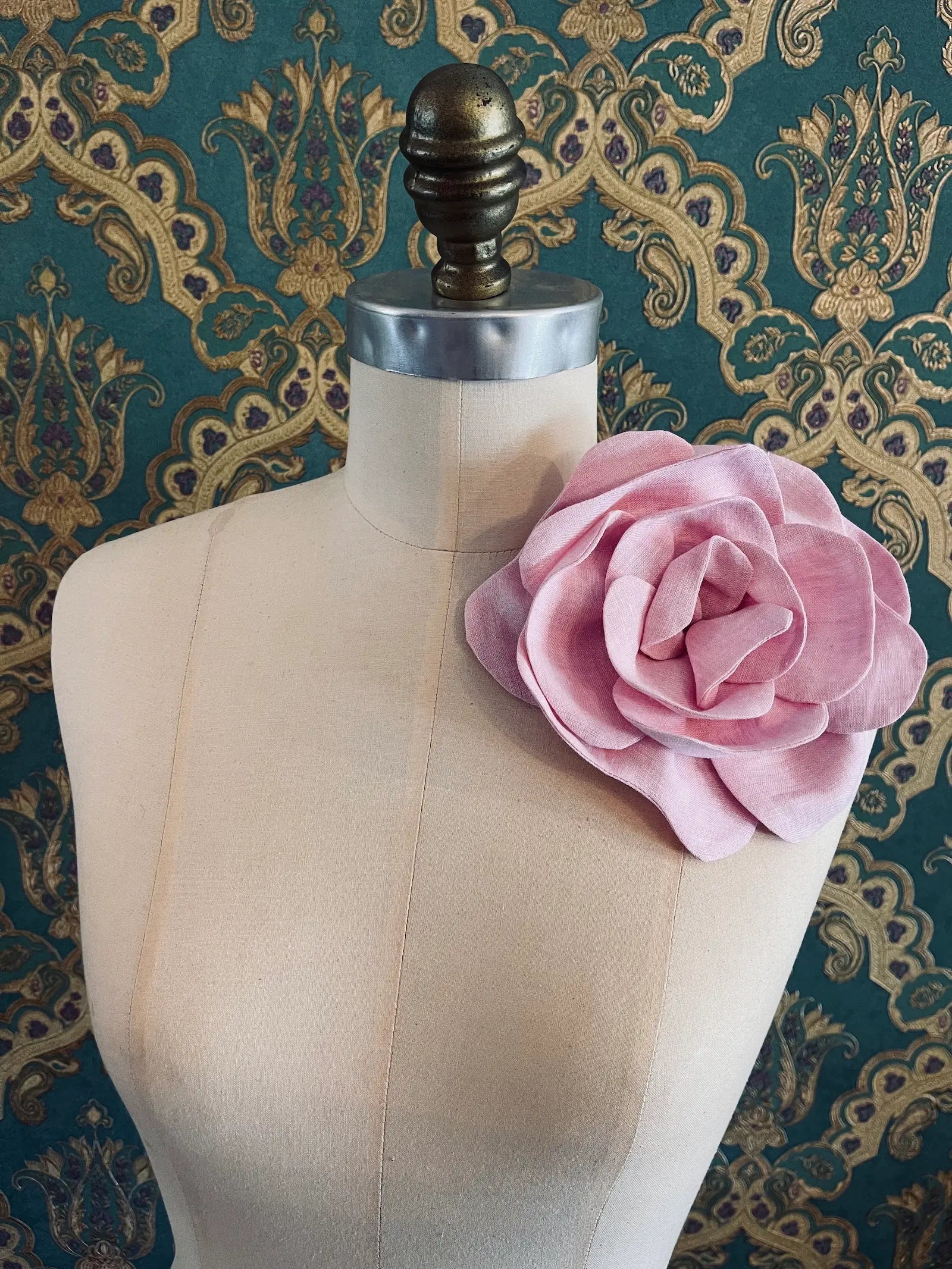 Broochella Florella large handmade linen flower brooch in pink. Pictured on a mannequin. The background is green and gold damask wallpaper.