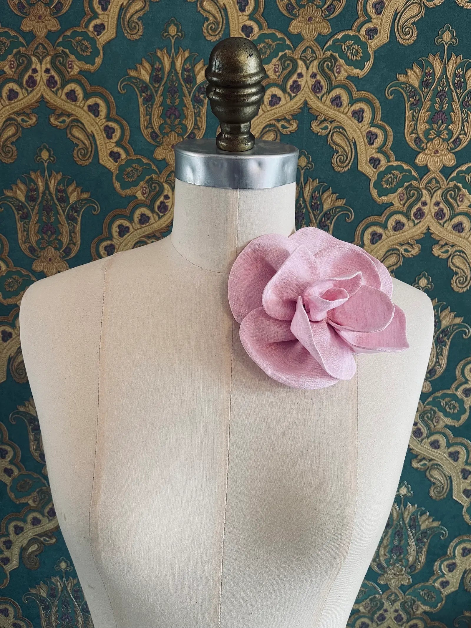 Broochella Florella small handmade linen flower brooch in pink. Pictured on a mannequin. The background is green and gold damask wallpaper.