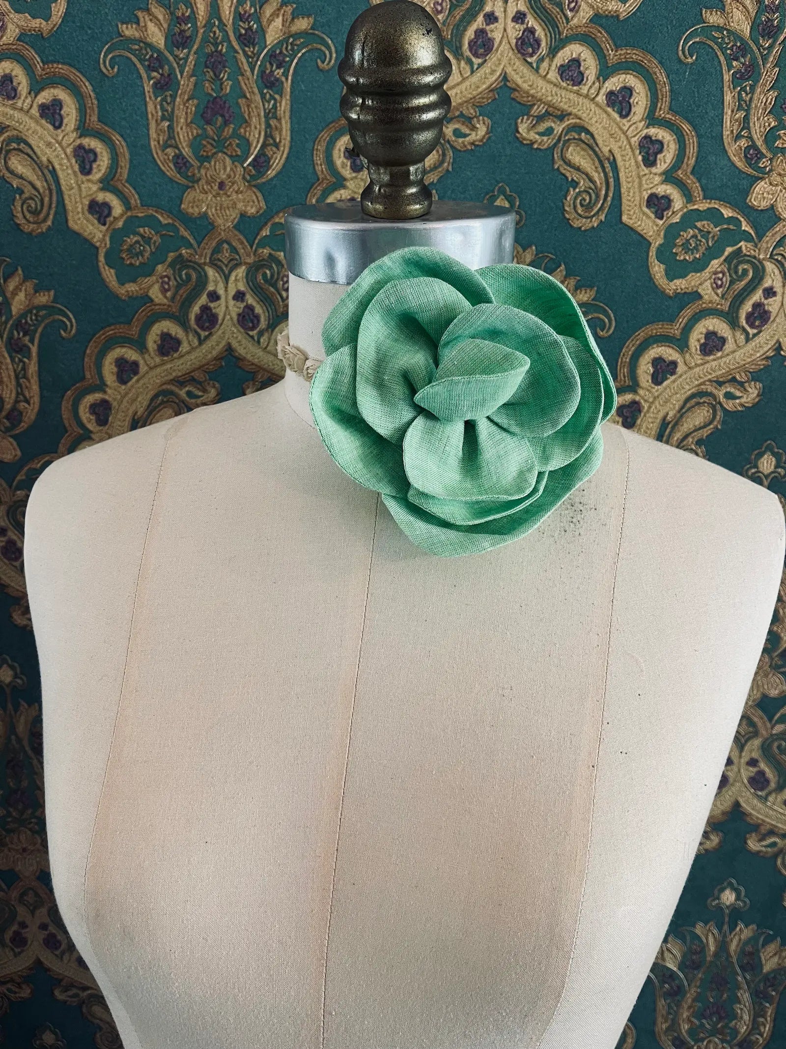 Broochella Florella small green handmade linen flower brooch and choker  Pictured on a mannequin. The background is green and gold damask wallpaper.