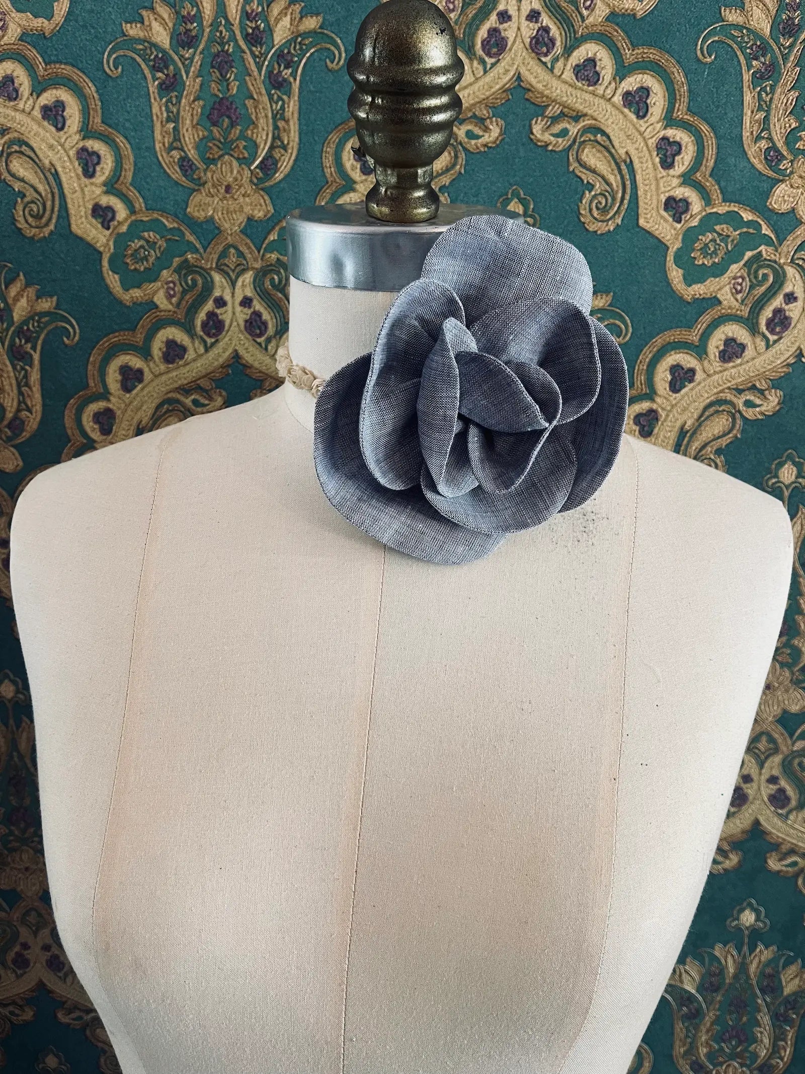 Broochella Florella small grey handmade linen flower brooch and choker  Pictured on a mannequin. The background is green and gold damask wallpaper.