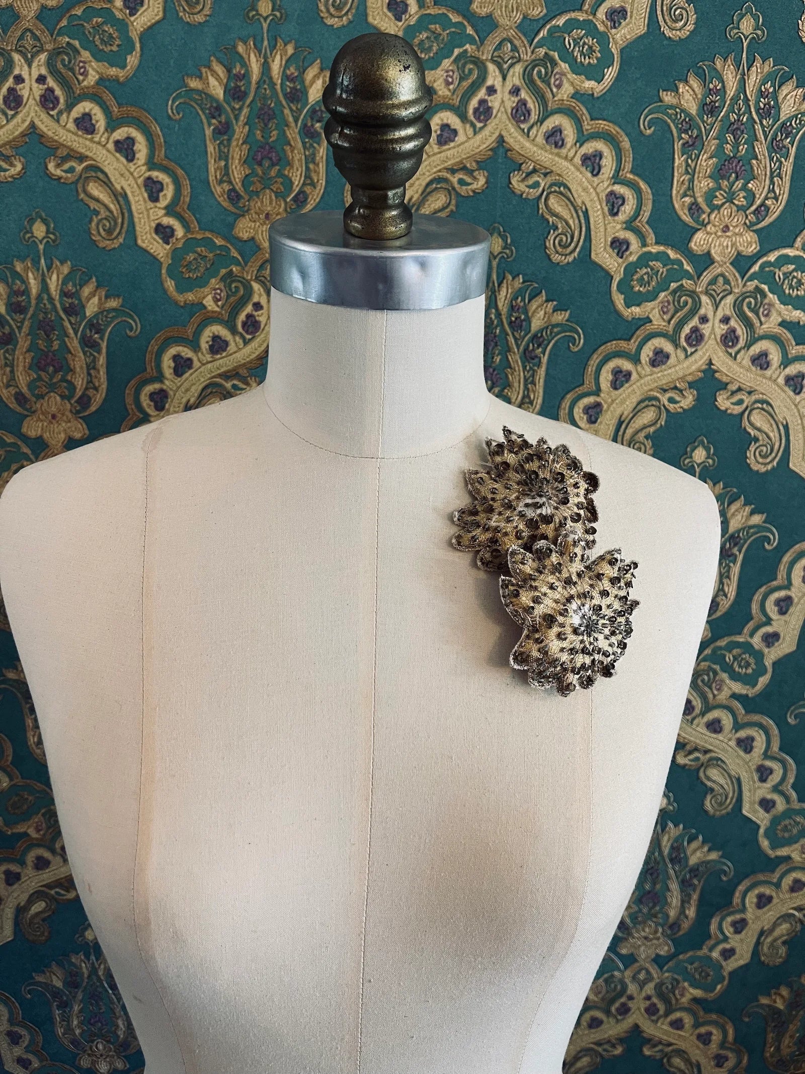 Broochella foglie d'autunno handmade flower brooch set. Pictured on a mannequin. The background is green and gold damask wallpaper