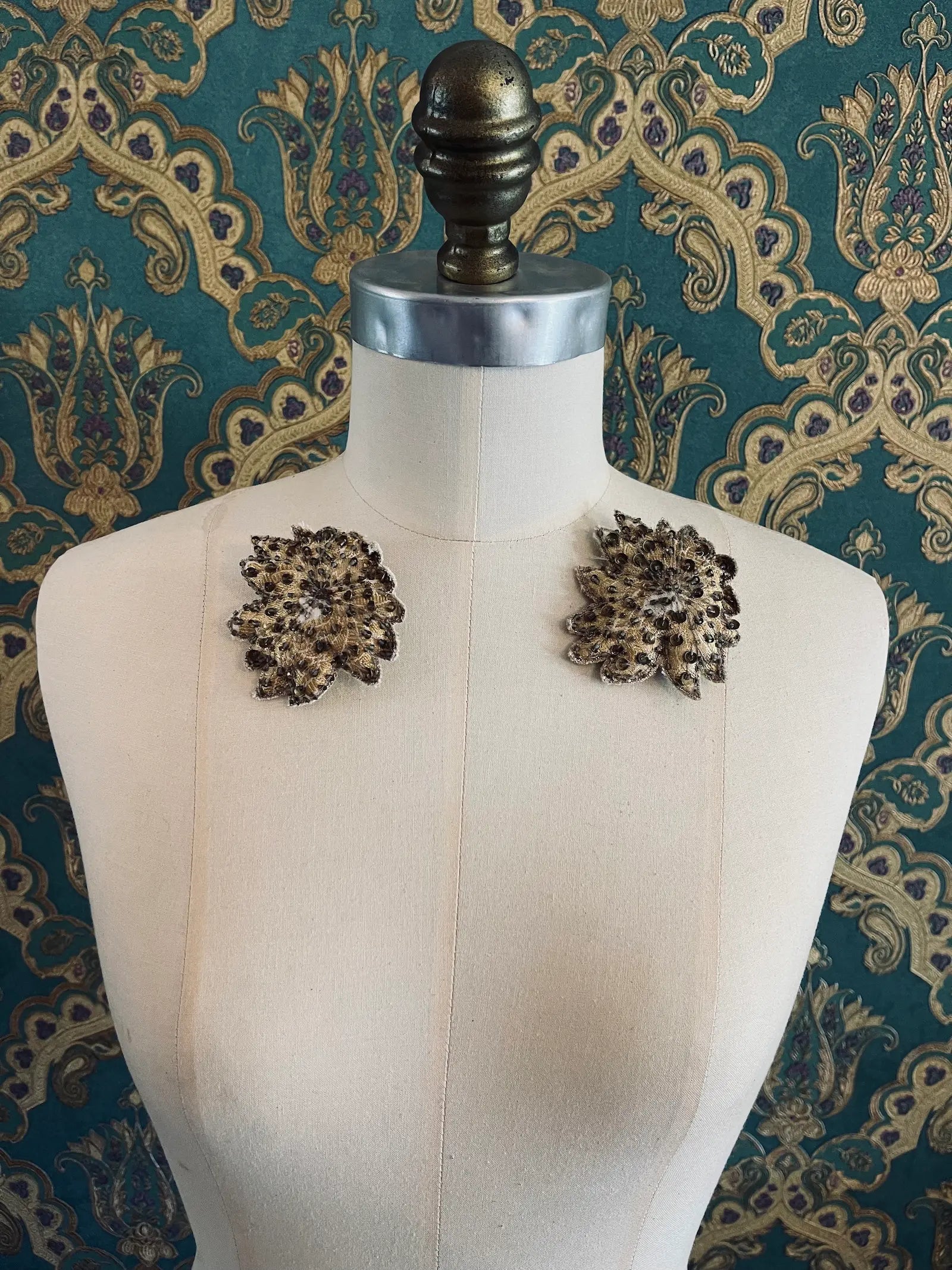 Broochella foglie d'autunno handmade flower brooch set. Pictured on a mannequin. The background is green and gold damask wallpaper.