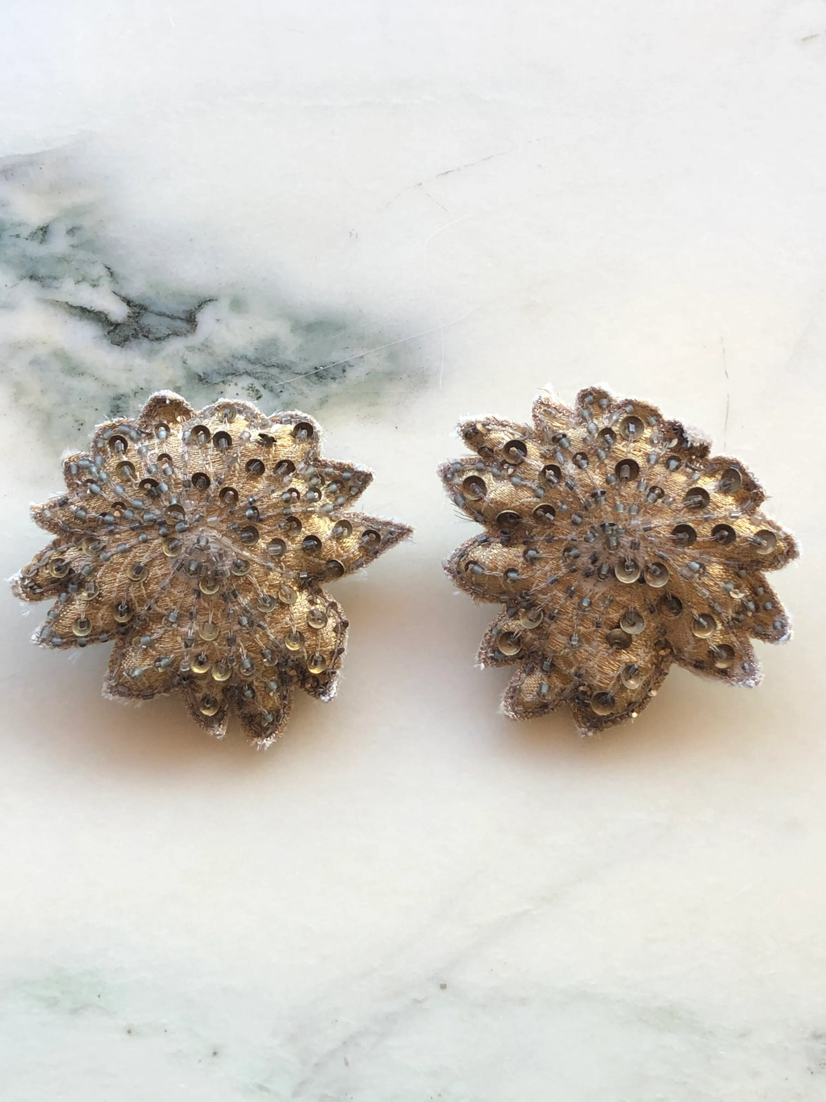 Broochella Men's Foglie d'Autunno Leaf Brooch Pin set featuring two layered gold-toned embroidered brooches embellished with sequins and beads, photographed on a white marble background with soft grey veining.