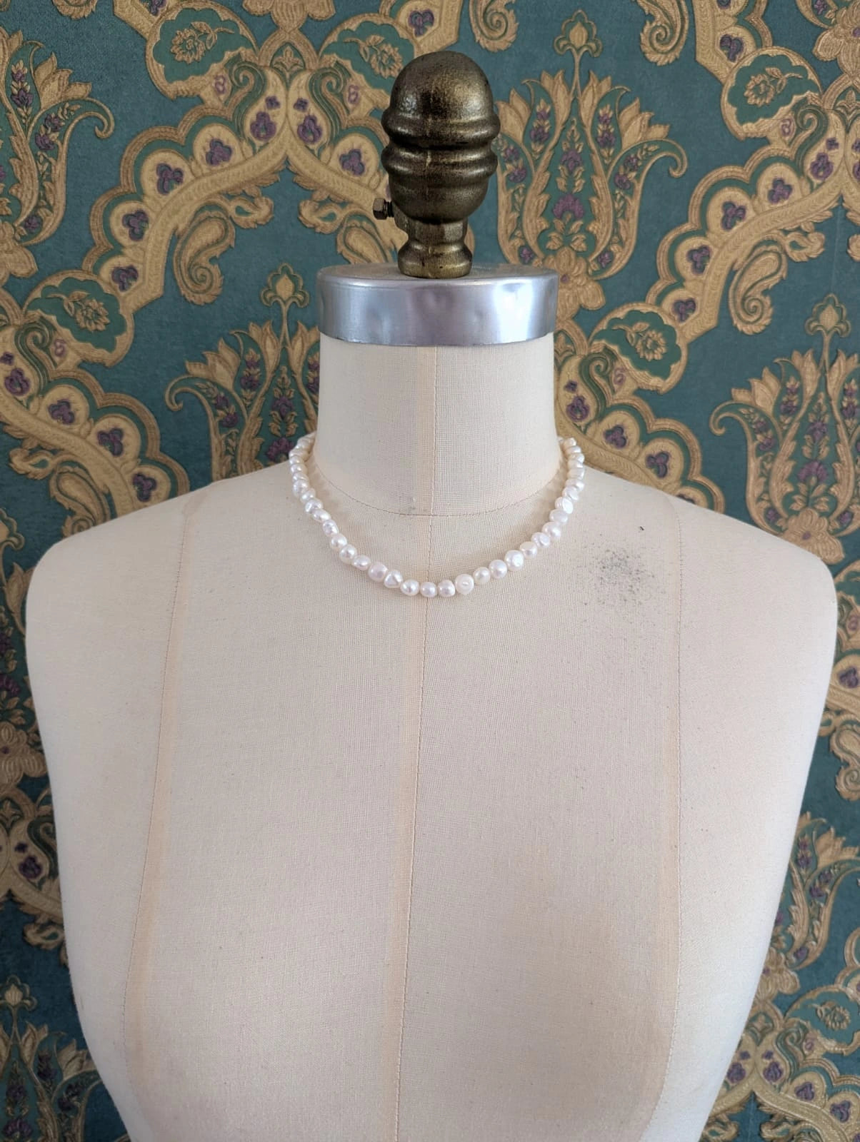Broochella freshwater pearl 45 cm necklace. It is pictured on a mannequin. The background is green and gold damask wallpaper.