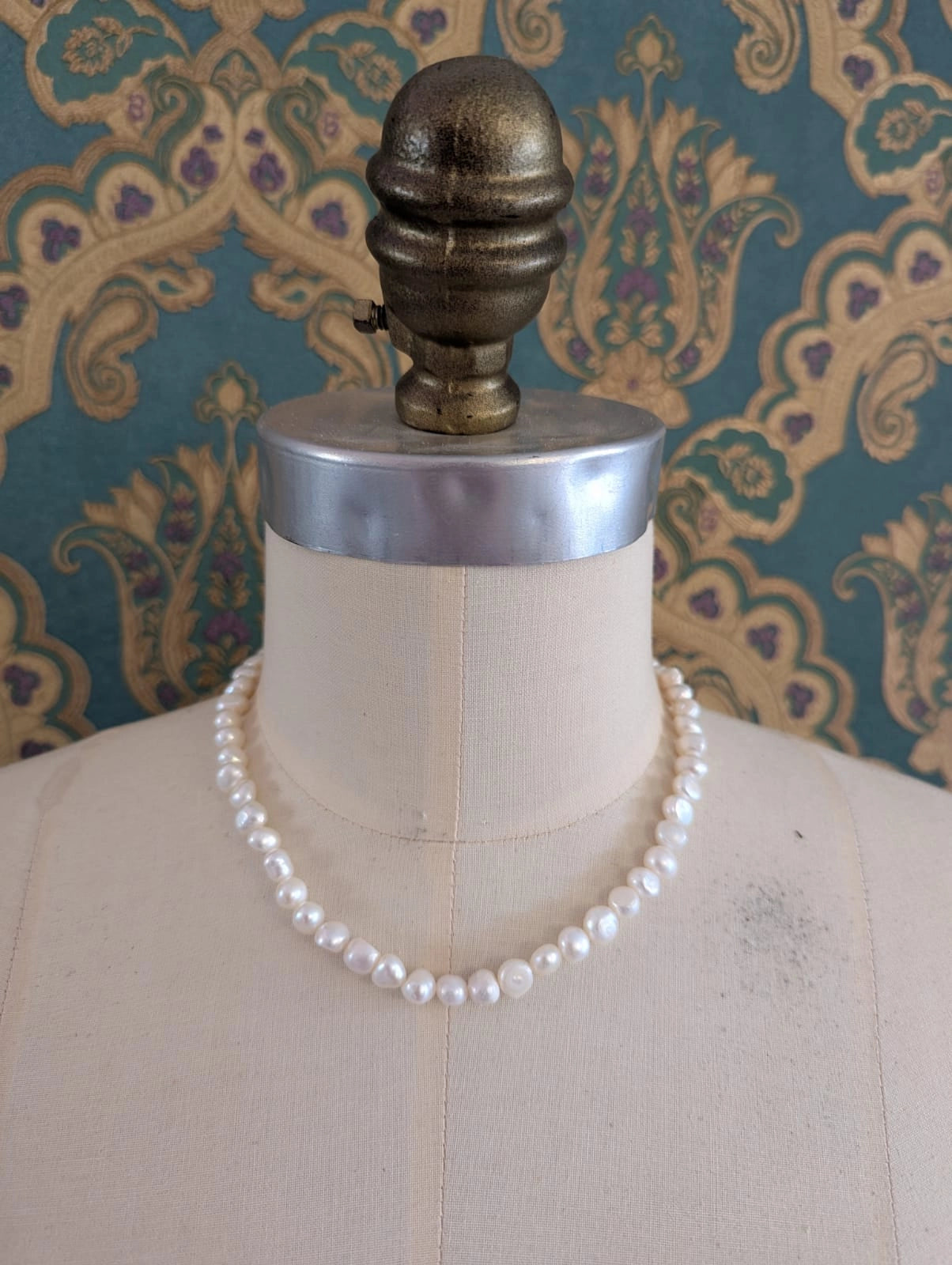Broochella freshwater pearl 45 cm necklace. It is pictured on a mannequin. The background is green and gold damask wallpaper.