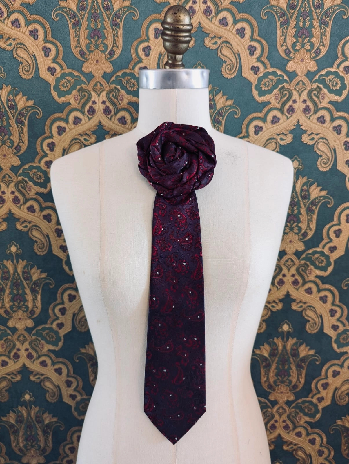 Broochella Fuente papotto vintage up-cycled vintage handcrafted rosette tie in burgundy and red damask. Pinned on a mannequin. The background is green and gold damask wallpaper