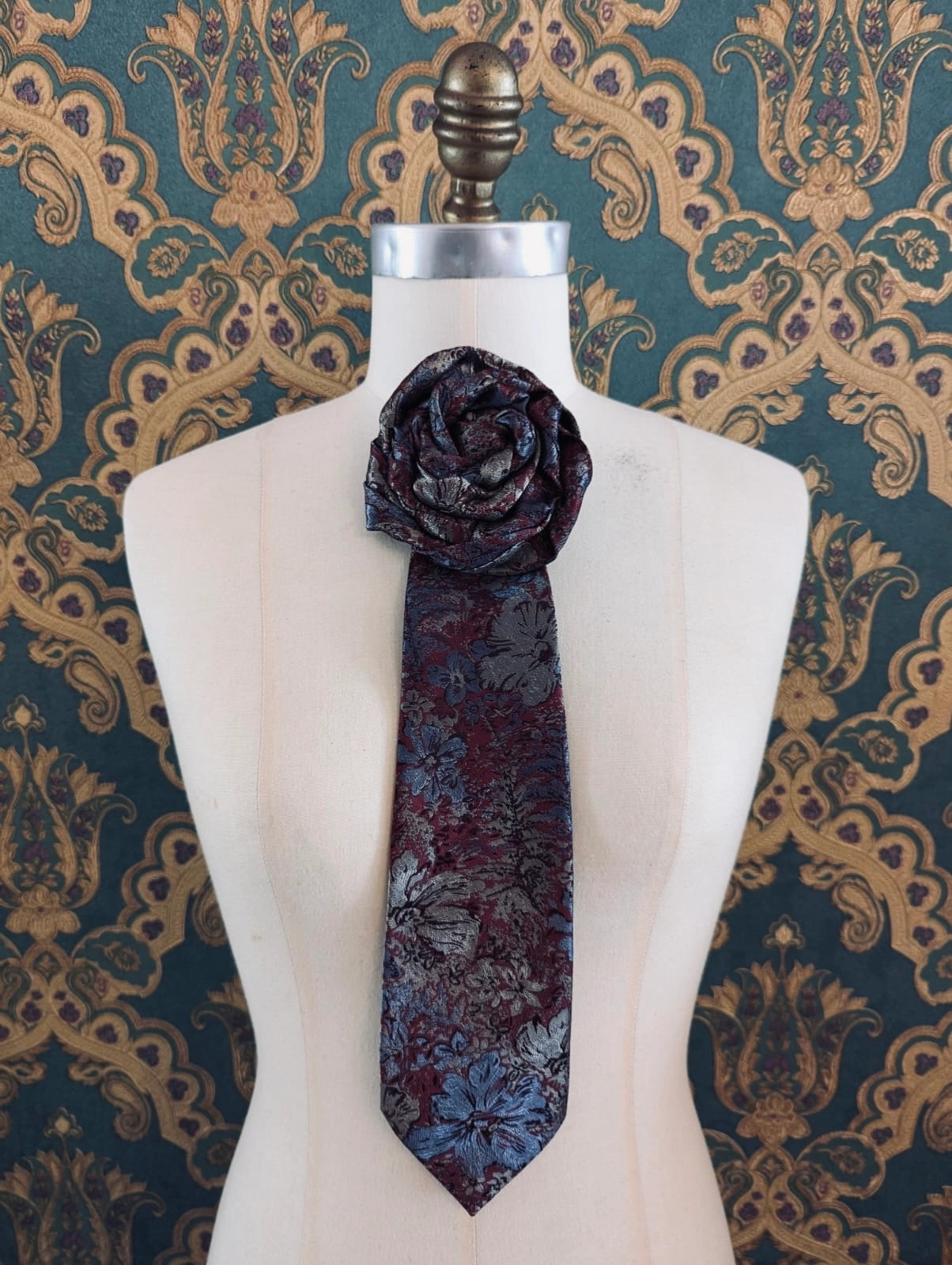 Broochella Fuente stefano vintage up-cycled vintage handcrafted rosette tie in burgundy and blue damask. Pinned on a mannequin. The background is green and gold damask wallpaper