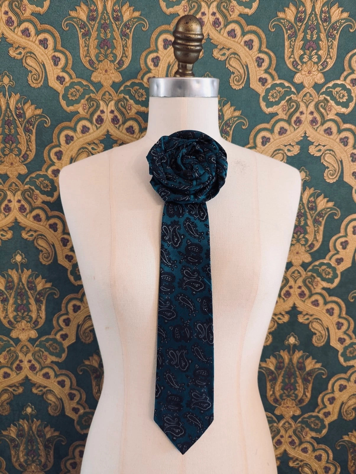 Broochella Fuente maurizio vintage up-cycled vintage handcrafted rosette tie in green and black paisley damask. Pinned on a mannequin. The background is green and gold damask wallpaper.