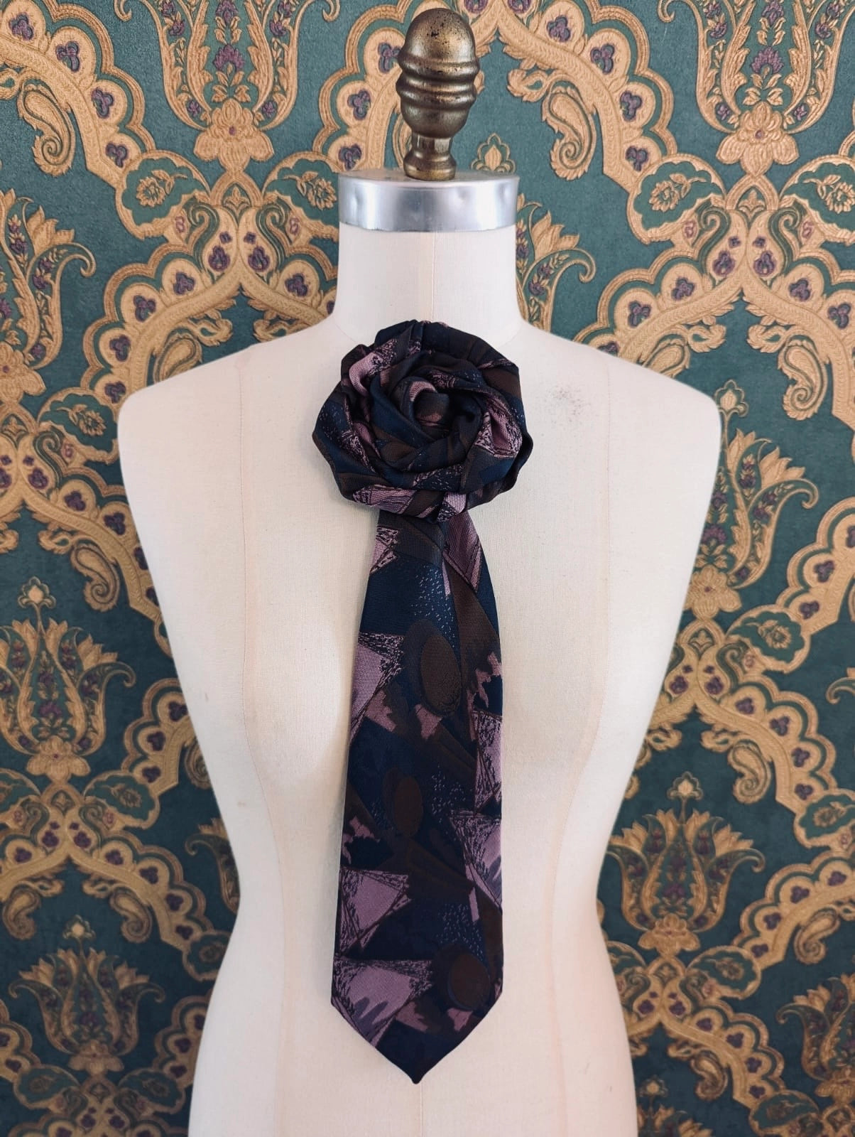 Broochella Fuente carmelo vintage up-cycled vintage handcrafted rosette tie in navy, pink and brown damask. Pinned on a mannequin. The background is green and gold damask wallpaper