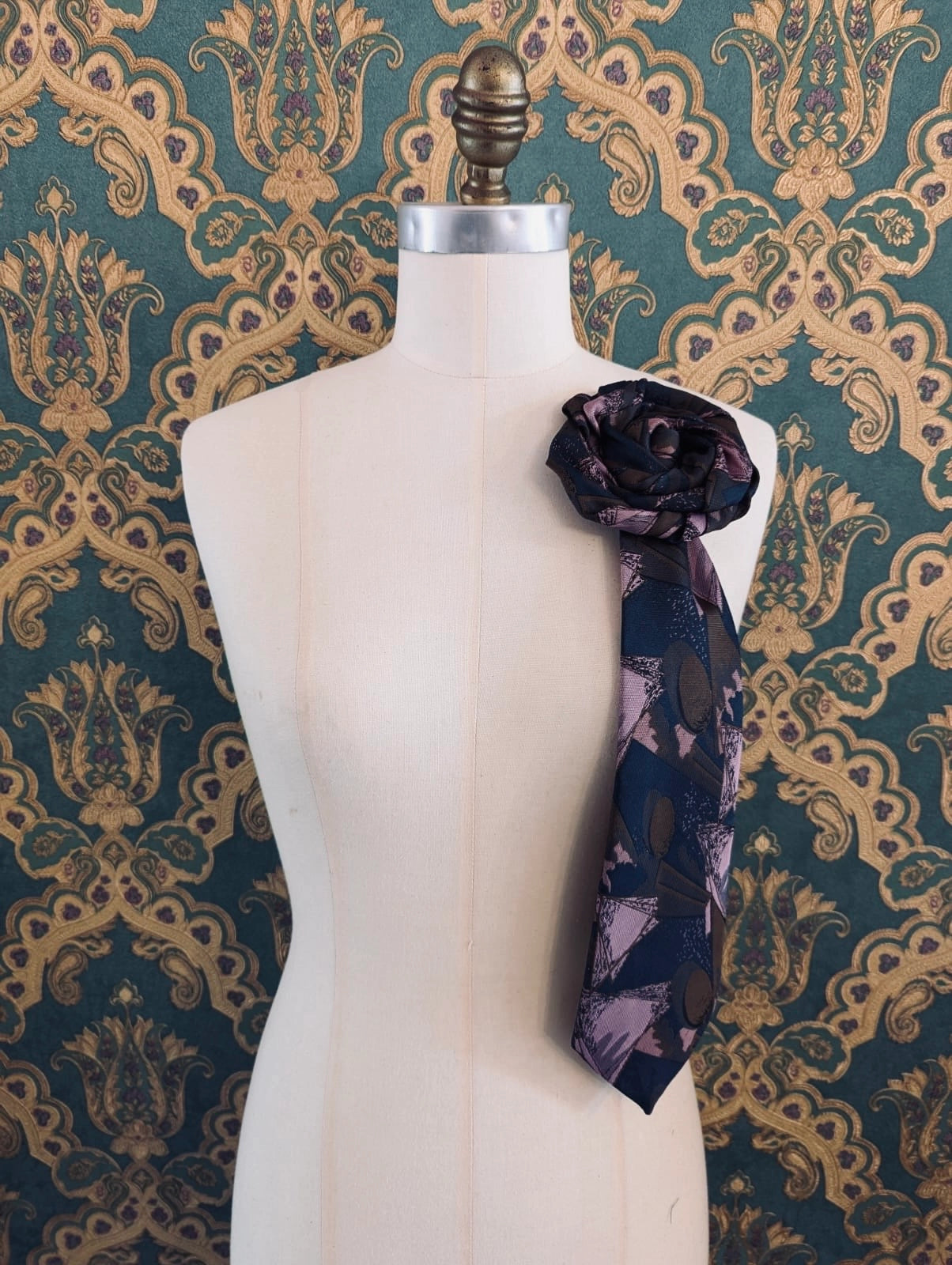 Broochella Fuente carmelo vintage up-cycled vintage handcrafted rosette tie in navy, pink and brown damask. Pinned on a mannequin. The background is green and gold damask wallpaper