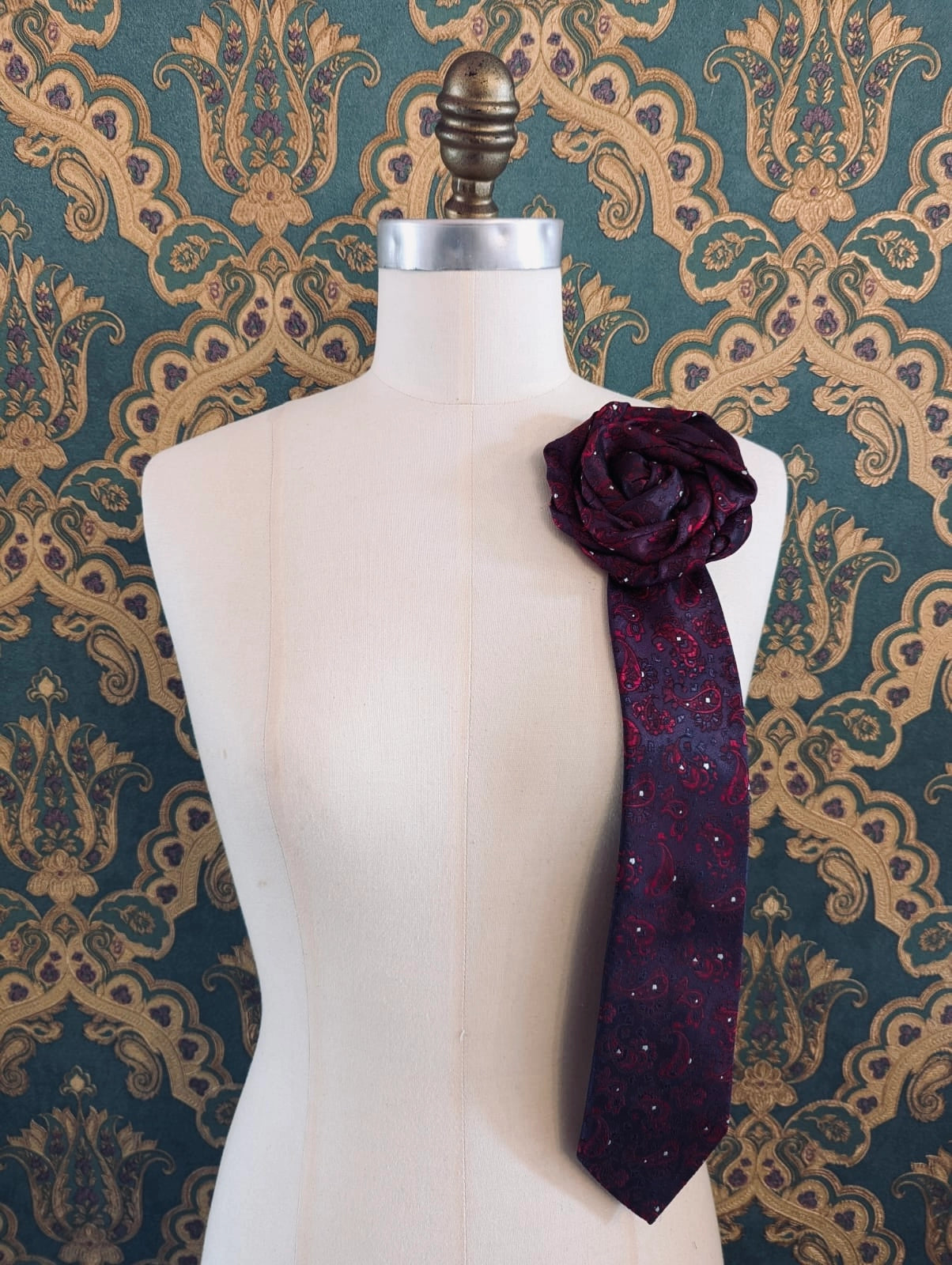 Broochella Fuente papotto vintage up-cycled vintage handcrafted rosette tie in burgundy and red damask. Pinned on a mannequin. The background is green and gold damask wallpaper