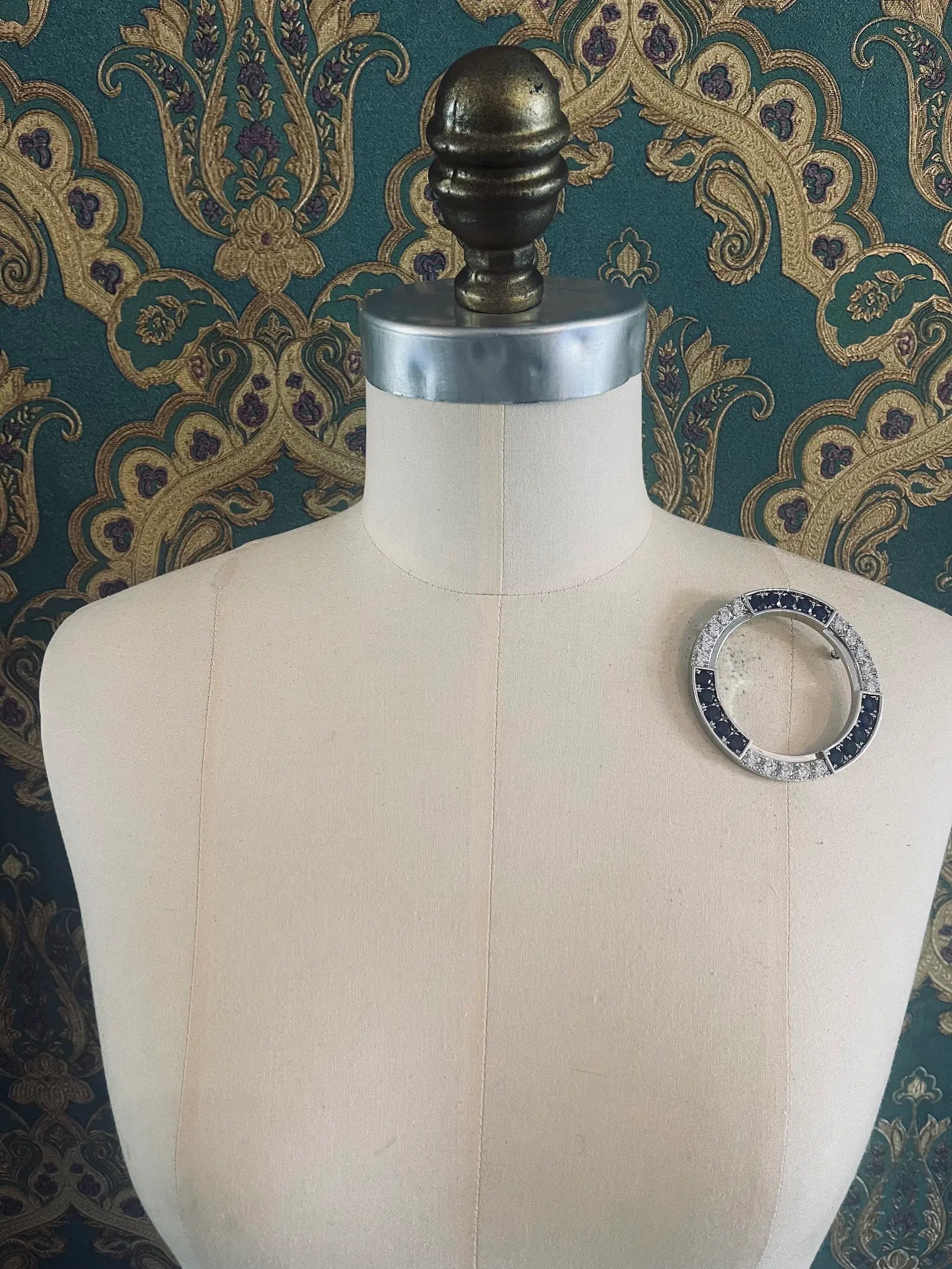 Broochella full moon silver metal brooch with silver and clear crystals. Pictured on a mannequin. The background is green and gold damask wallpaper