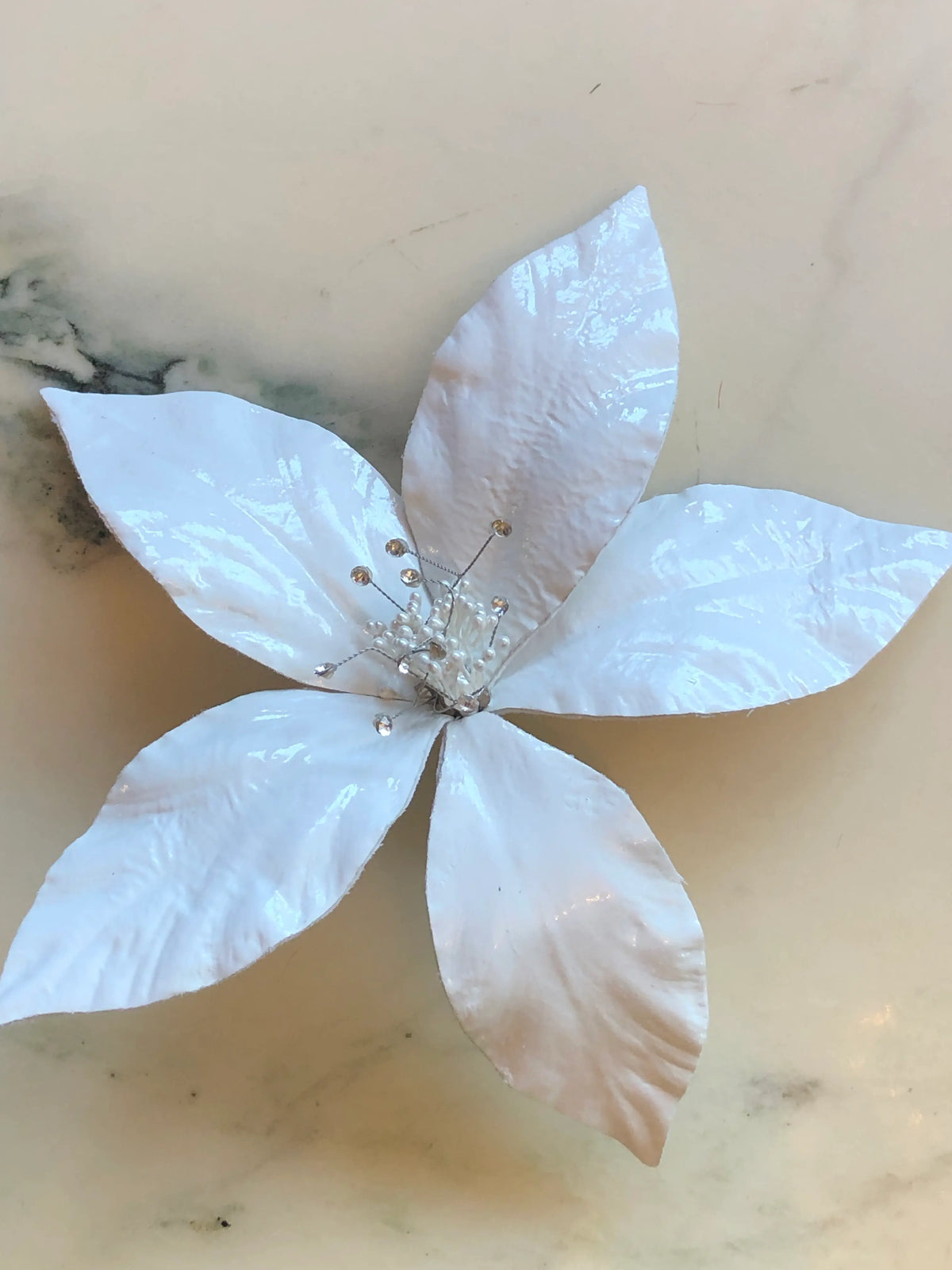 Broochella Giglio Bridal Brooch featuring five sculptural pearlescent white petals with delicate pearl and crystal detailing at the centre, photographed on a pale cream marble background.
