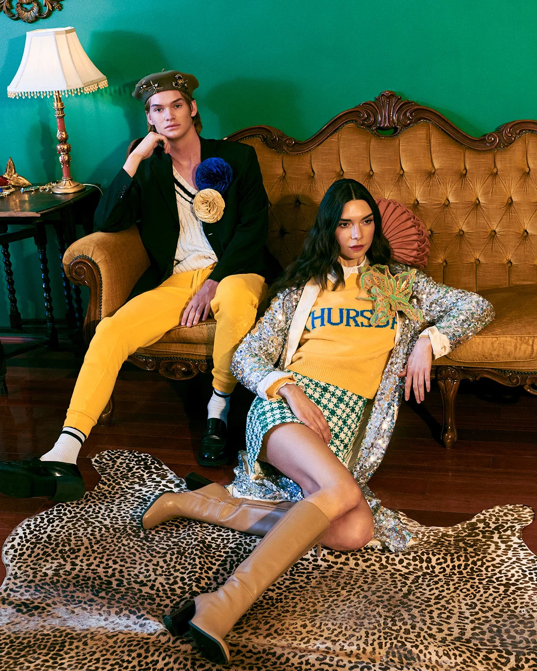 A fashion editorial photo featuring a male and female model in retro 1960s-inspired outfits. The man wears a black blazer, white shirt, yellow trousers, and a beret.