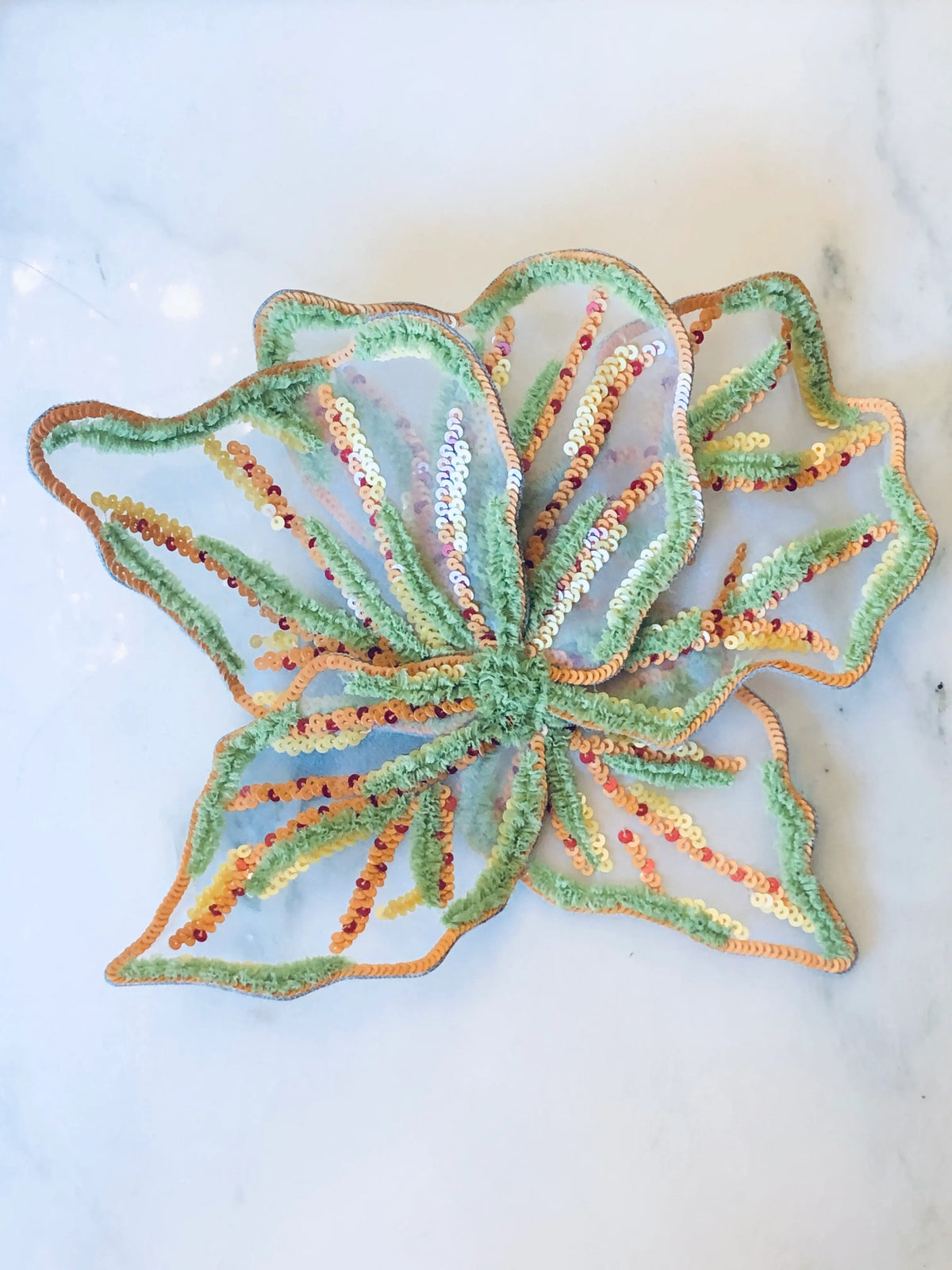 Broochella Giglio di Tigre Flower Brooch Pin - Large in green, featuring sculptural sheer petals embellished with mint green, peach and gold sequins and textured embroidery on a cream marble background.