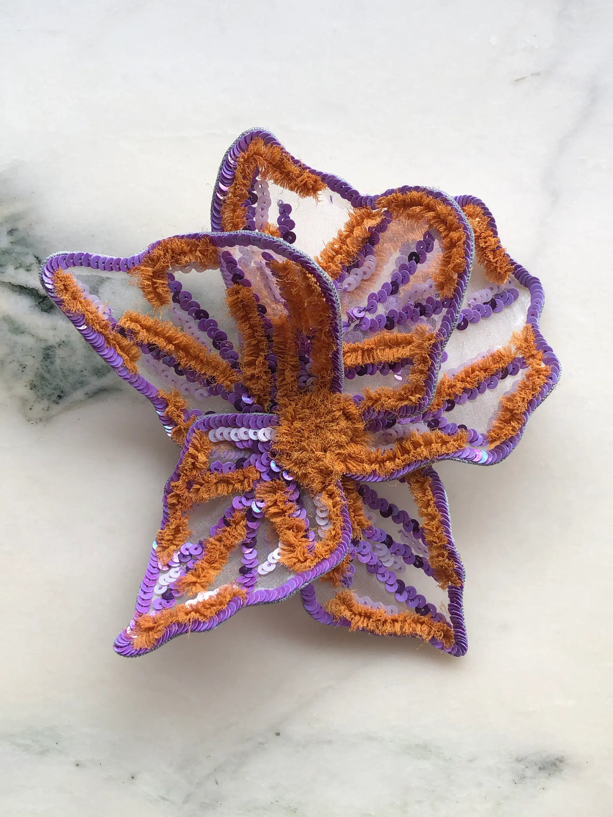 Broochella Men's Giglio di Tigre Small Flower Brooch Pin in purple, featuring layered sheer petals decorated with lilac and violet sequins, contrasting burnt orange textured embroidery and a dimensional floral centre. A colourful statement flower brooch for blazers, dresses and creative styling.