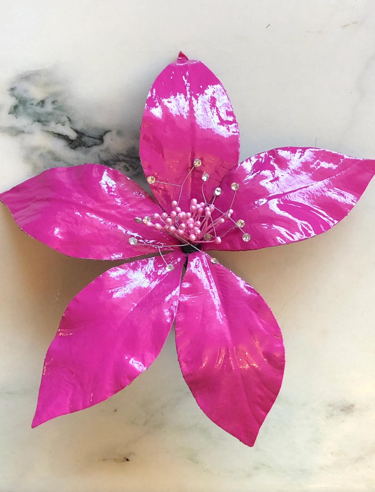 Broochella Men's Giglio Flower Brooch Pin in glossy pink, featuring sculptural leather lily petals with a textured black centre and delicate crystal-tipped stamens on a cream marble background.