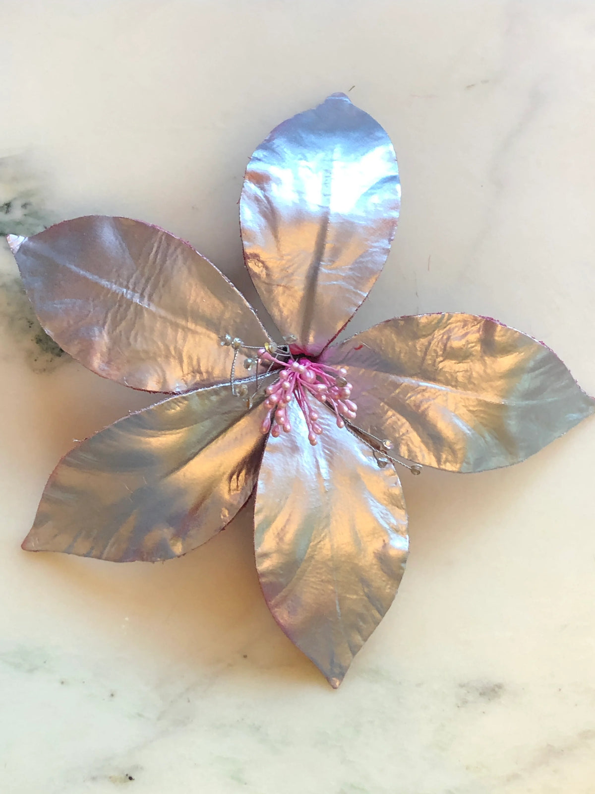 Broochella Men's Giglio Flower Brooch Pin in glossy silver, featuring sculptural leather lily petals with a textured black centre and delicate crystal-tipped stamens on a cream marble background.