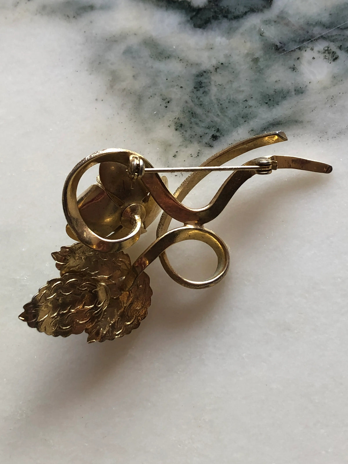 Broochella Gilded Bouquet vintage gold-tone brooch featuring sculptural flowers, layered petals and curling stems, measuring approximately 4 × 6 cm. Photographed on white and grey marble.