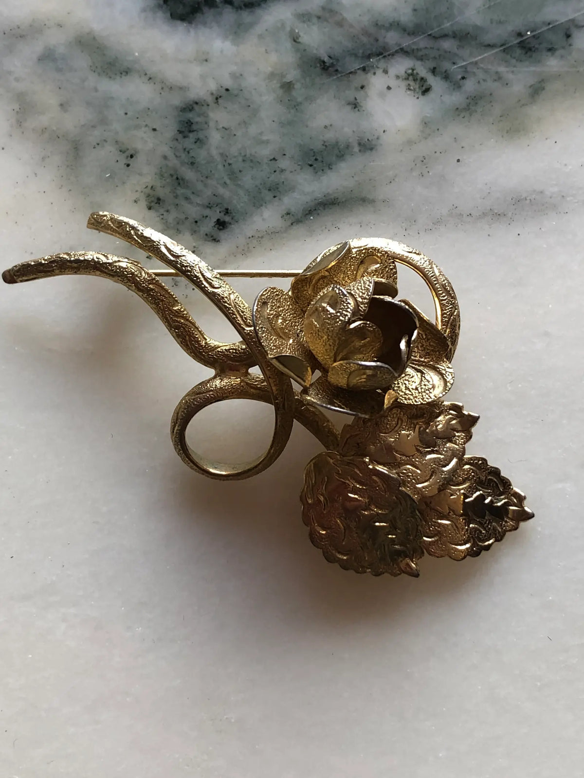 Broochella Gilded Bouquet vintage gold-tone brooch featuring sculptural flowers, layered petals and curling stems, measuring approximately 4 × 6 cm. Photographed on white marble